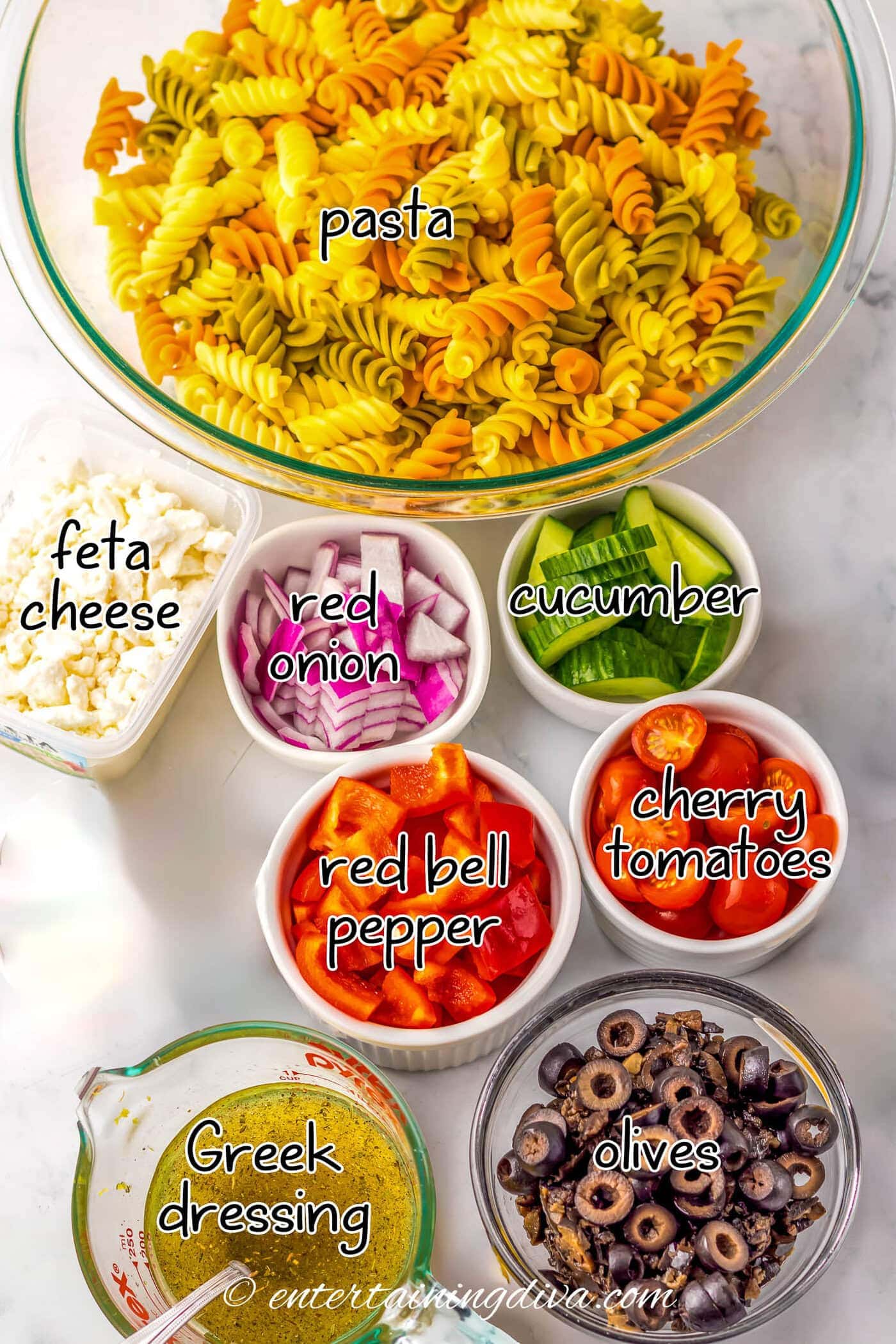 Greek pasta salad ingredients - pasta, feta cheese, red onion, cucumber, red bell pepper, cherry tomatoes, olives and Greek dressing