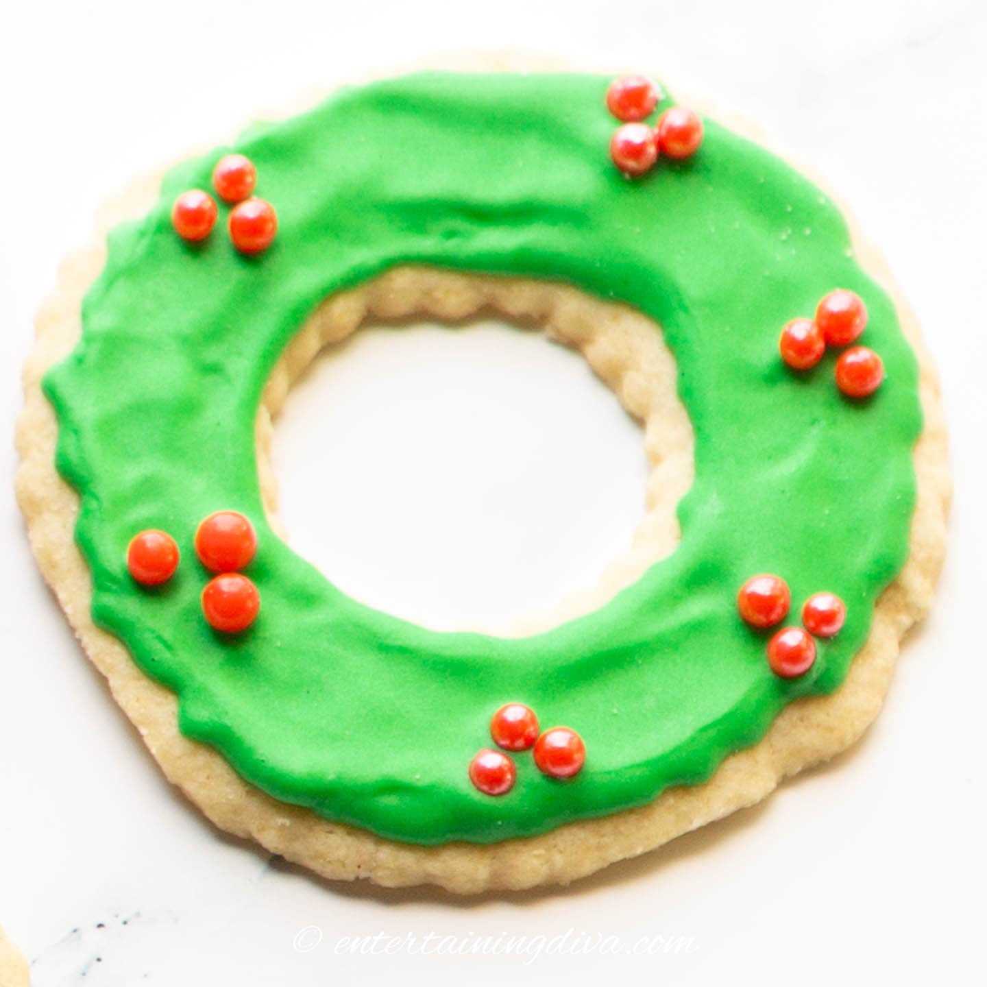 Wreath sugar cookie decorated with green royal icing and red sugar balls