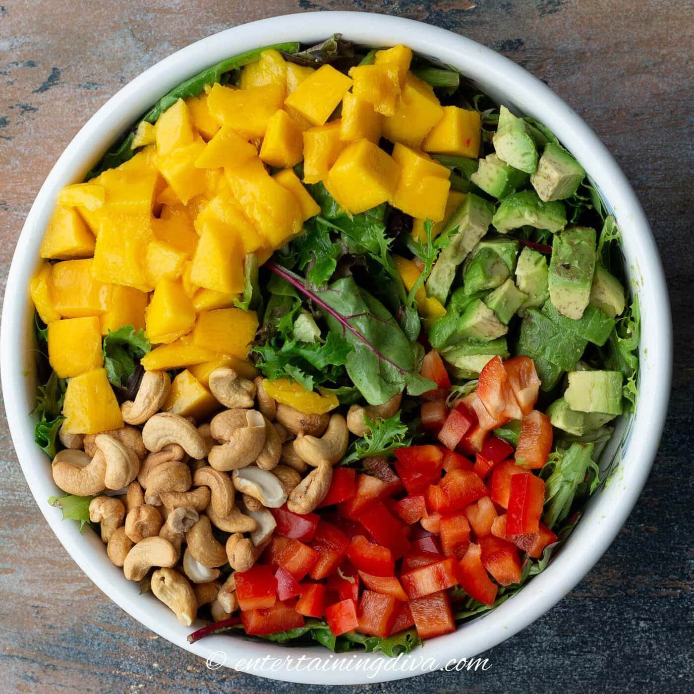 mango, avocado, red peppers, cashews and mixed salad greens in a bowl