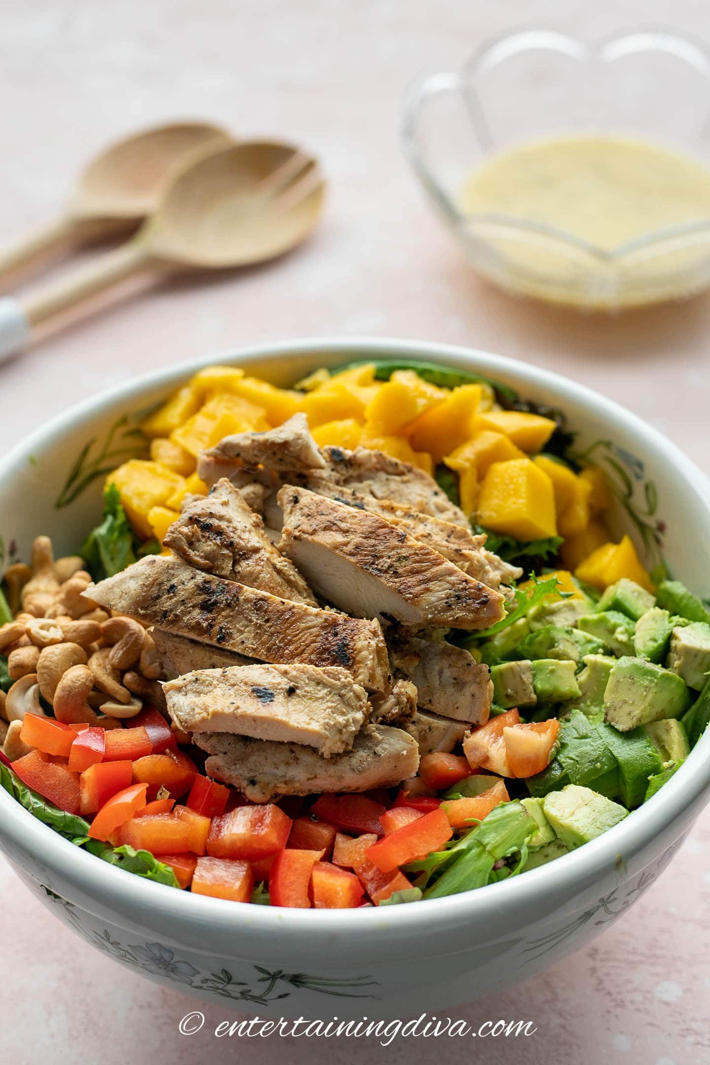 grilled chicken avocado and mango salad in a bowl with salad dressing and spoons in the background