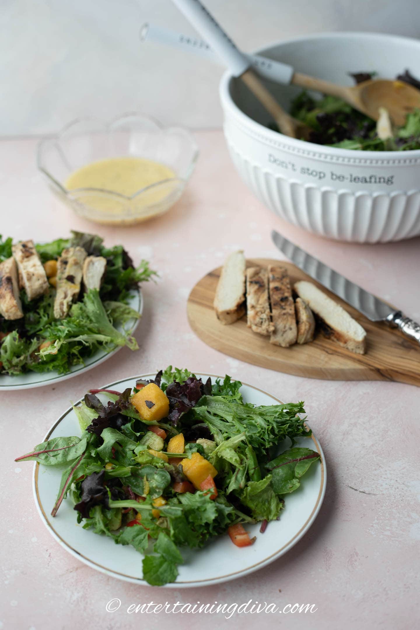 Grilled chicken mango avocado salad on a plate with sliced chicken on a cutting board and a bowl of salad behind it