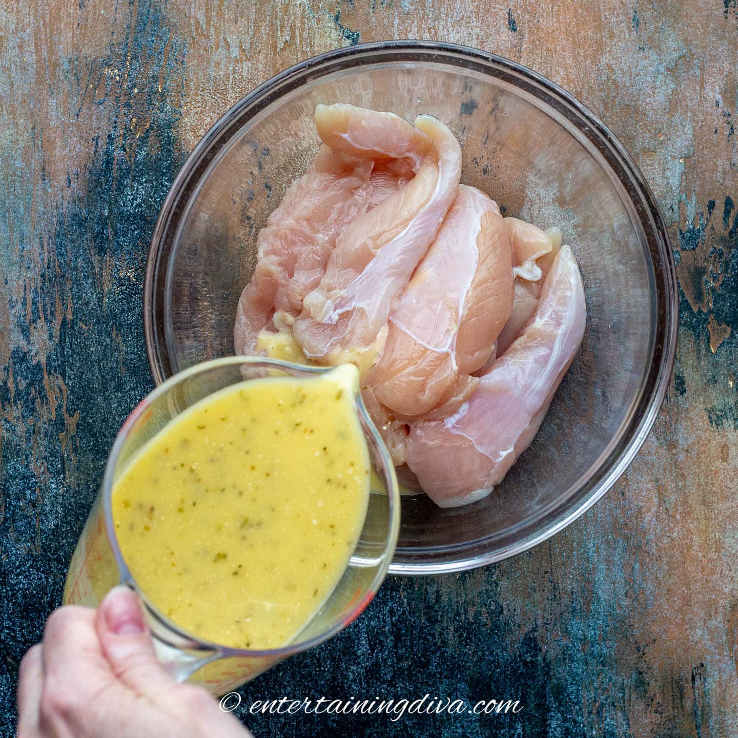 chicken in a bowl with marinade being poured in
