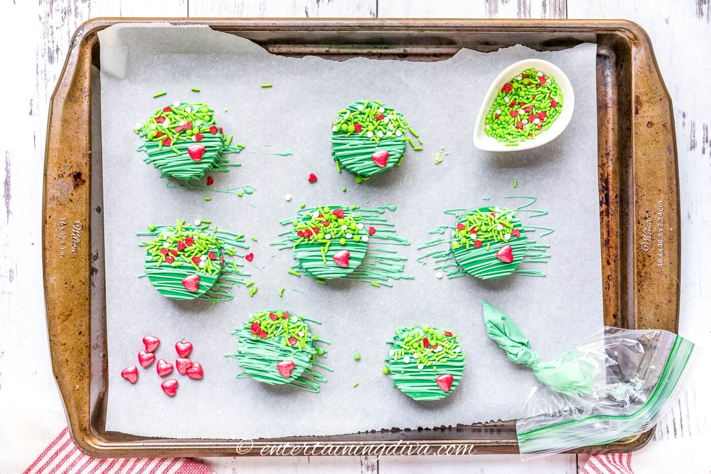 Decorated Grinch cake pucks on a baking sheet with sprinkles and green chocolate