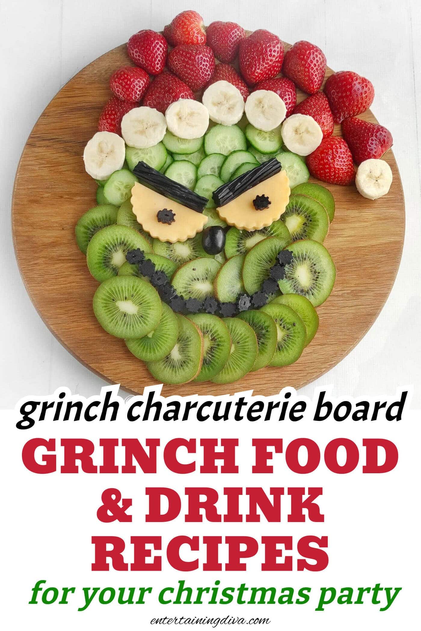 A round wooden board with sliced kiwi, cucumber, bananas, strawberries, and cheese arranged to resemble the Grinch's face.