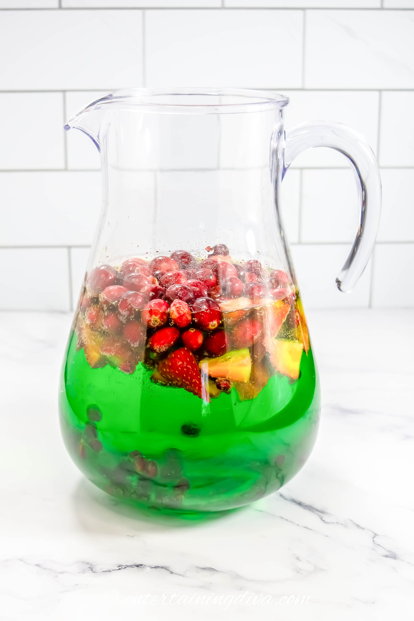 white wine, midori and pineapple juice in a pitcher with cranberries, strawberries, green apples and pomegranate arils