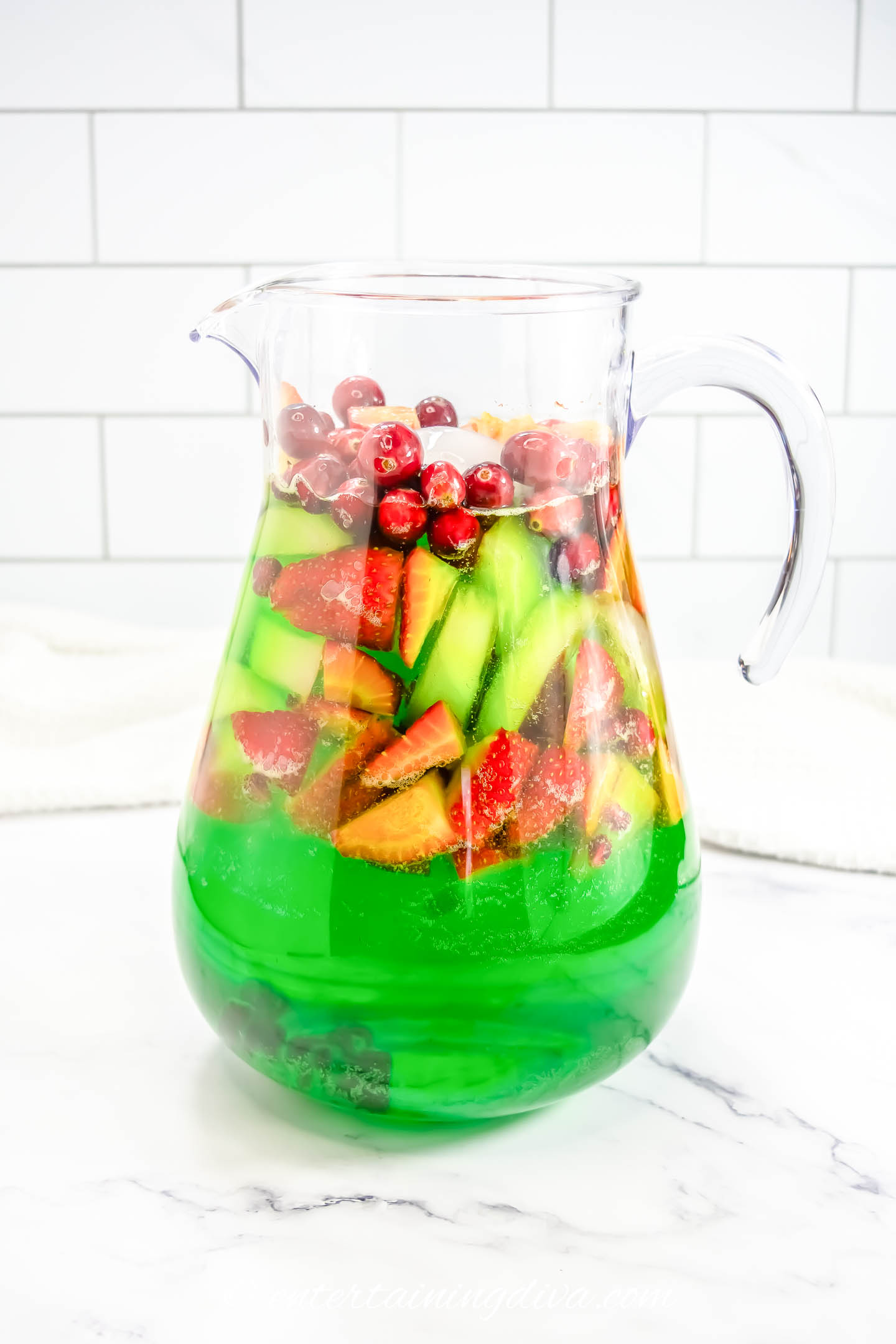 white wine, midori, pineapple juice and sprite in a pitcher with cranberries, strawberries, green apples and pomegranate arils