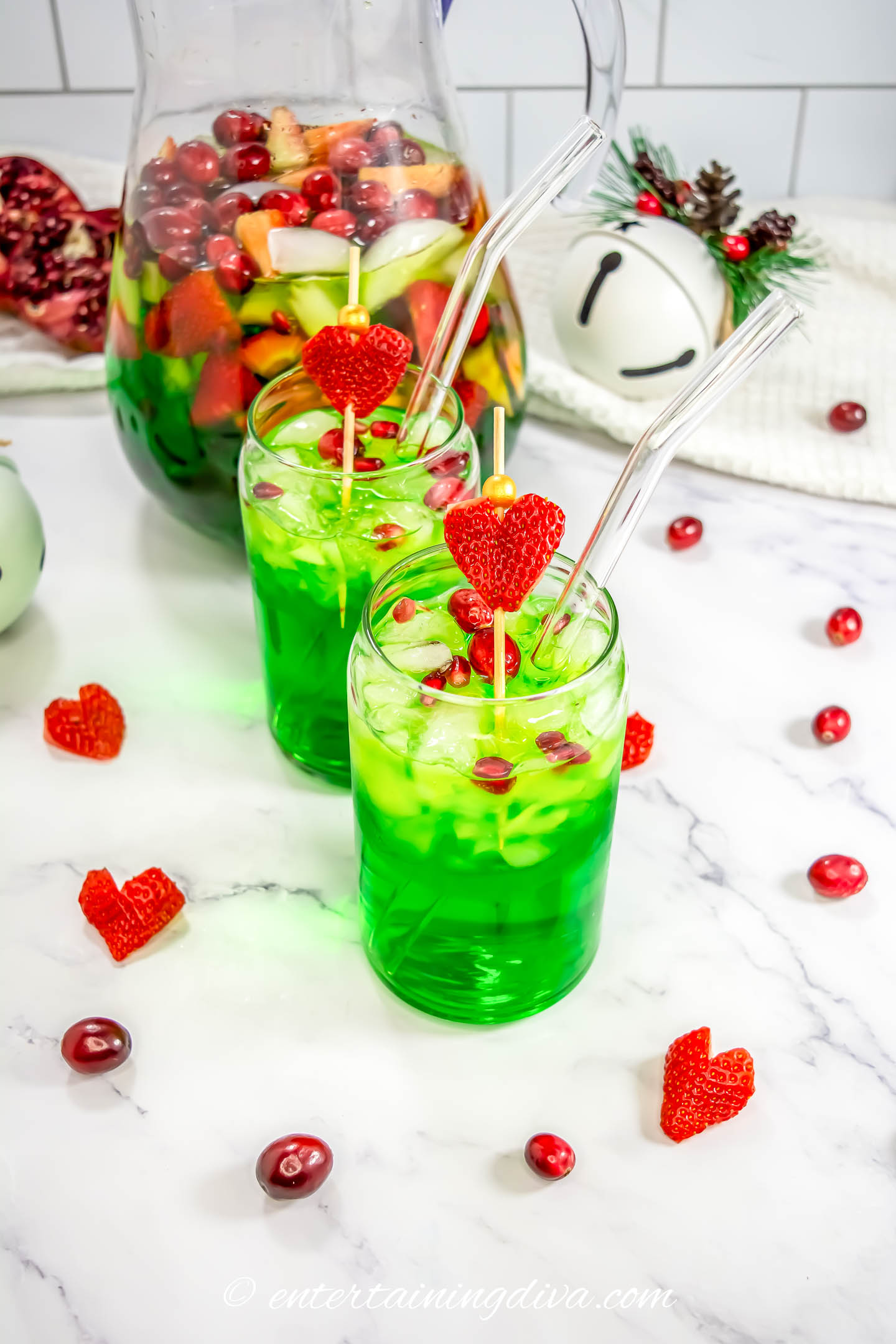 Two glasses of Grinch sangria with strawberry heart garnish in front of a pitcher of the sangria