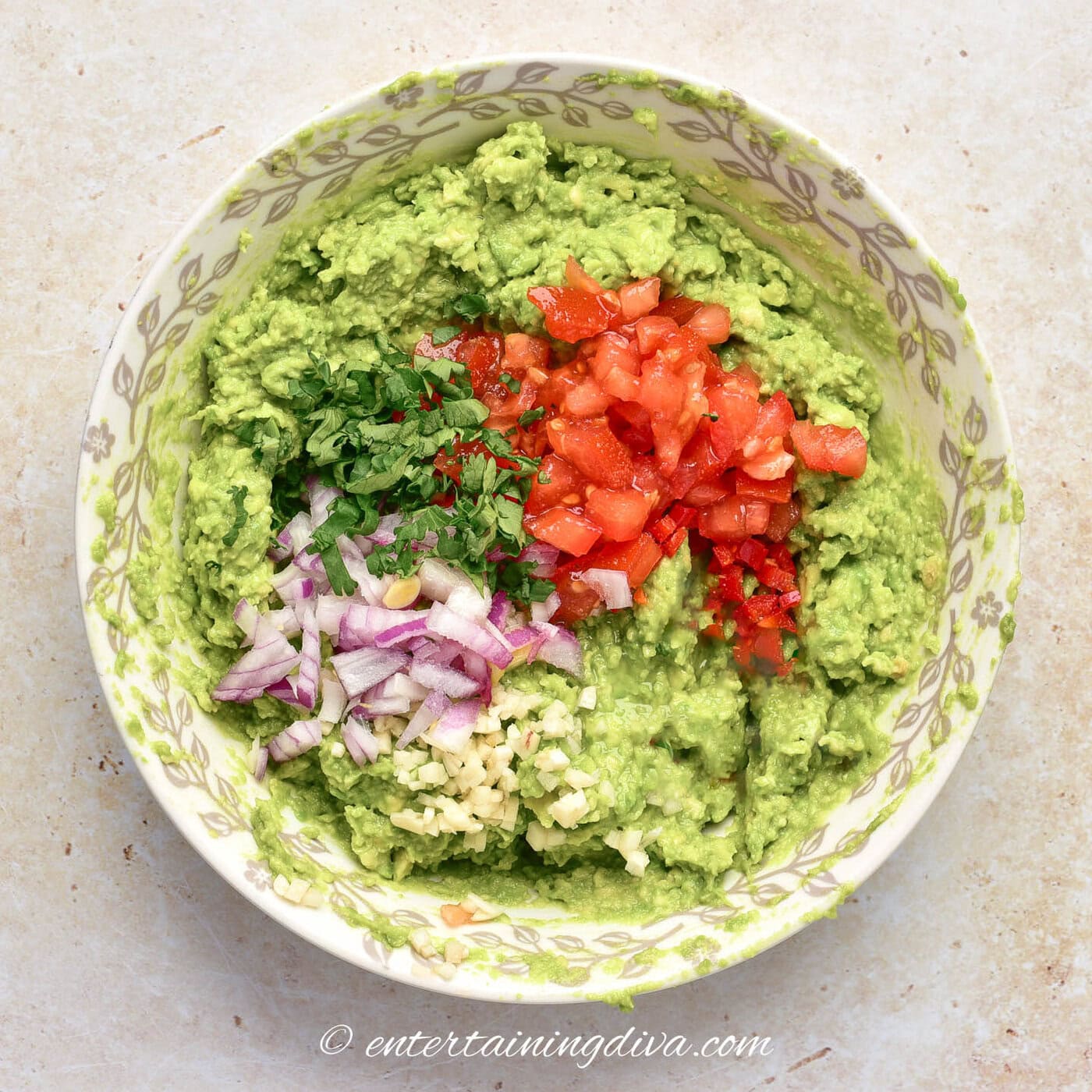 mashed avocado in a bowl with tomatoes, cilantro, red onion and garlic