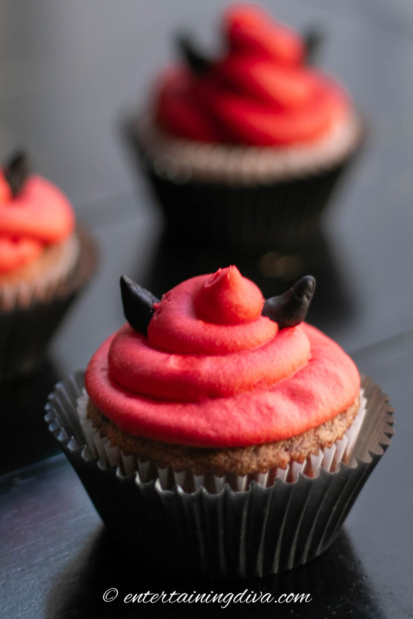 Red velvet Halloween cupcakes decorated with red icing and black fondant horns like the devil