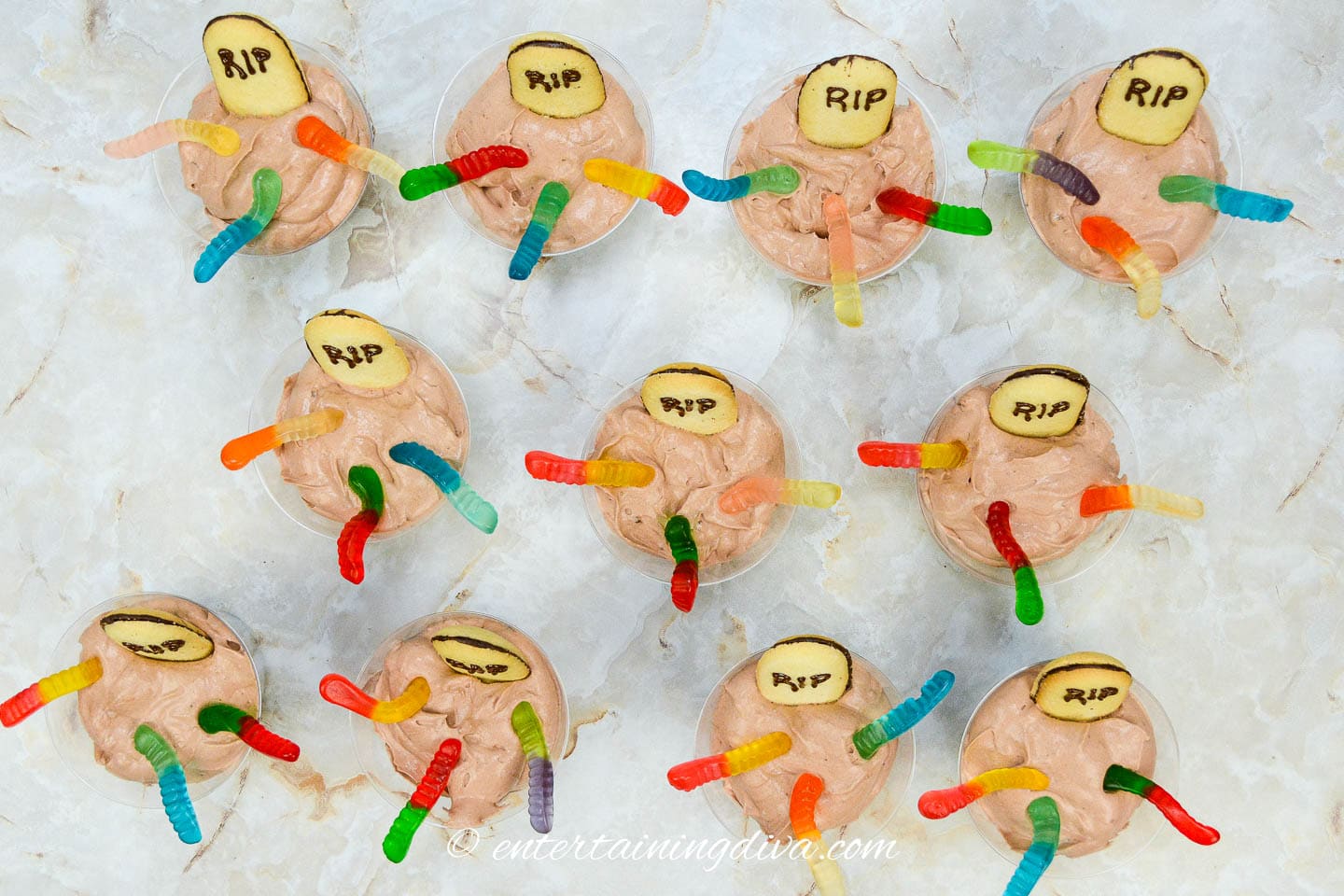 A group of Halloween graveyard pudding cups with tombstone cookies and gummy worms on them
