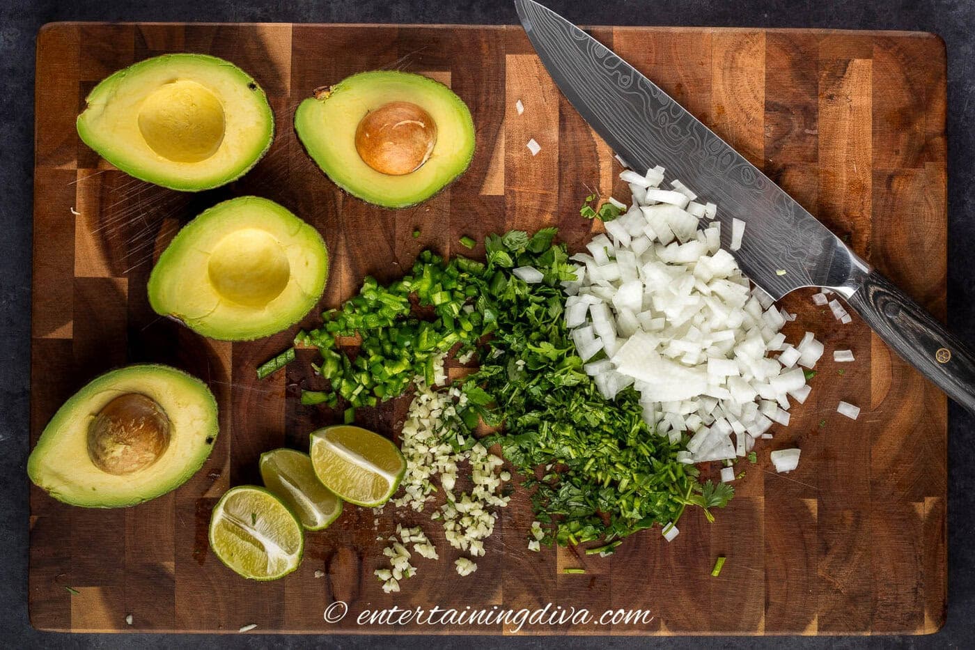 Chopped onions, cilantro, jalapeno peppers, limes, avocado and minced garlic on a cutting board with a chefs knife