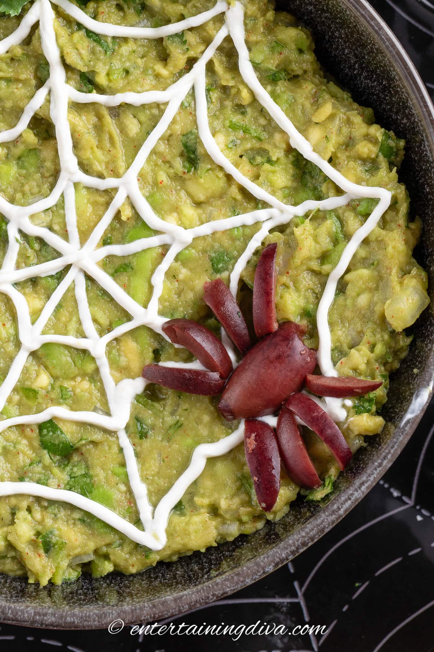 close up of Halloween guacamole with an olive spider on a sour cream spider web