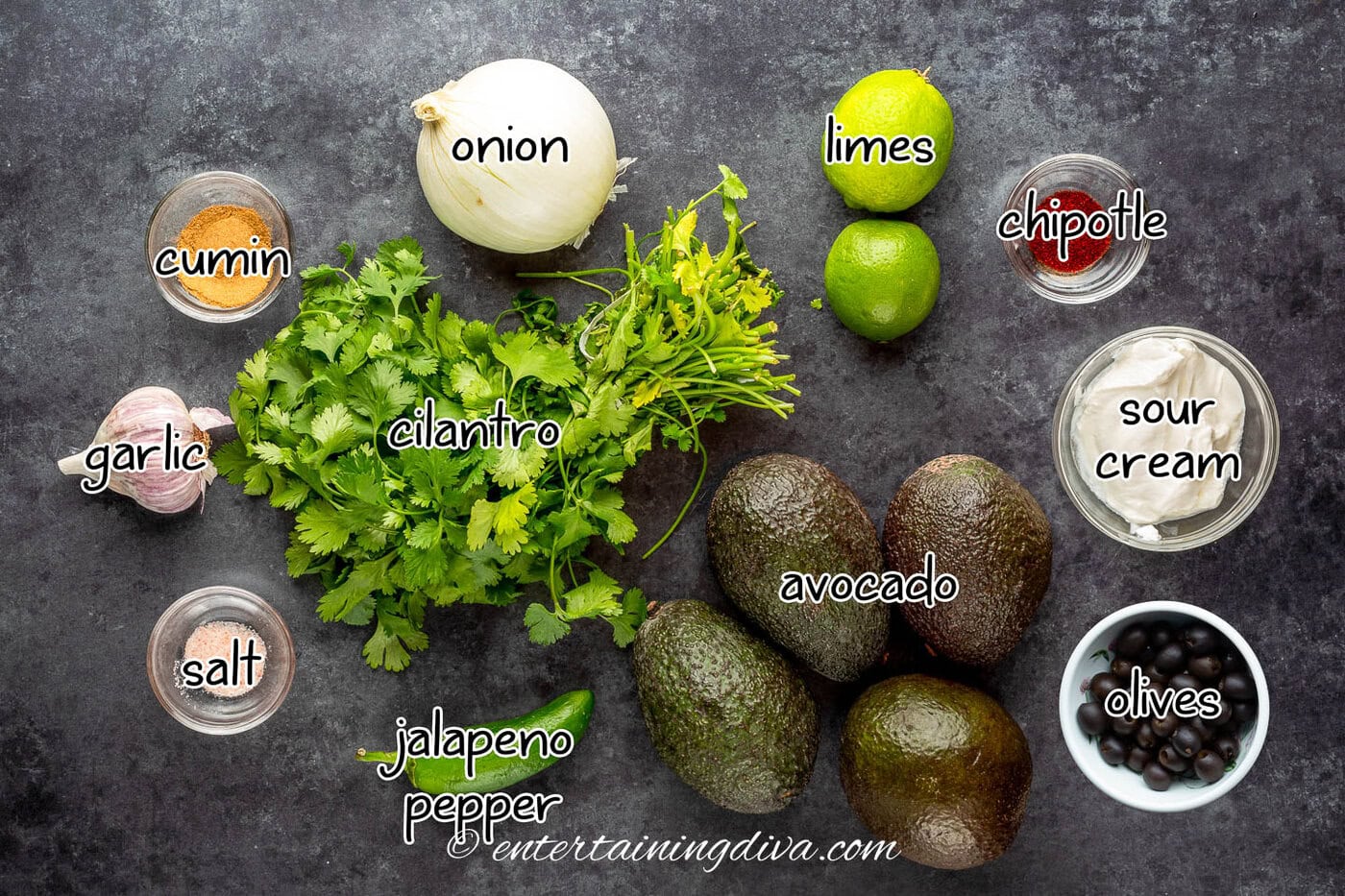 Halloween guacamole ingredients - avocado, cilantro, jalapeno pepper, salt, garlic, cumin, onion, limes, chipotle, sour cream and olives