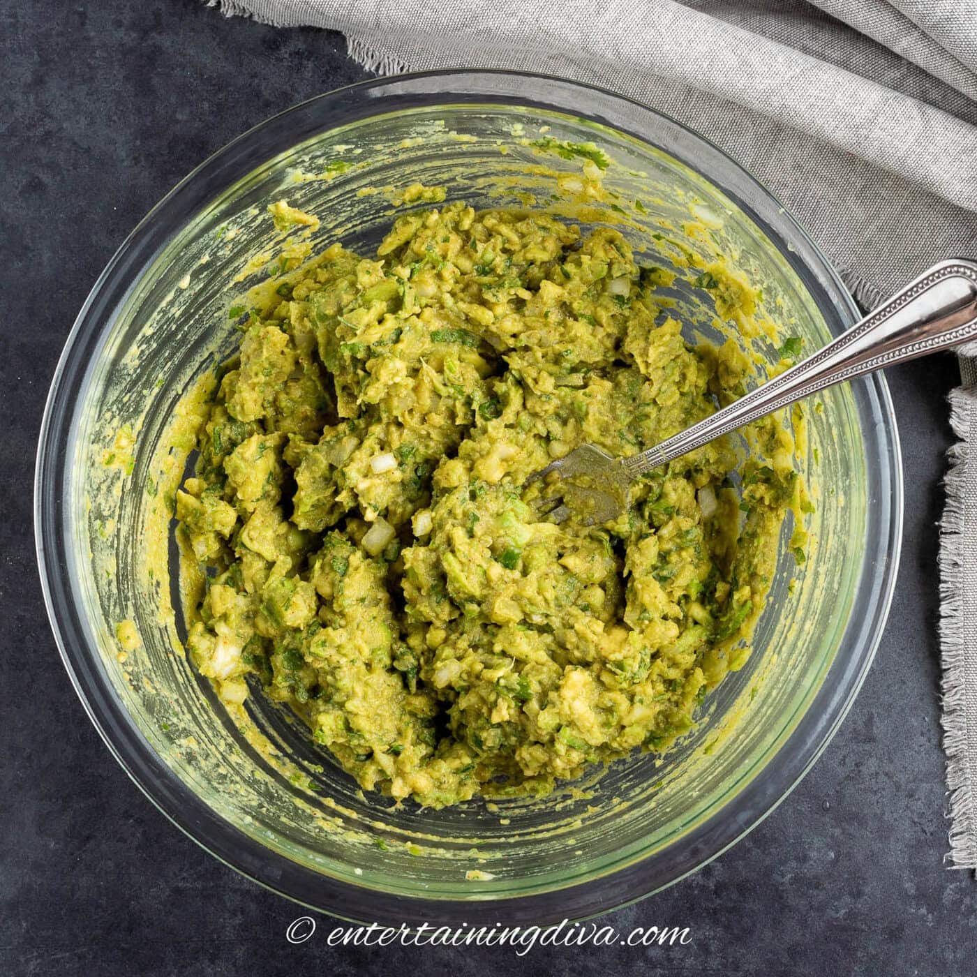Guacamole being mashed with a fork in a bowl
