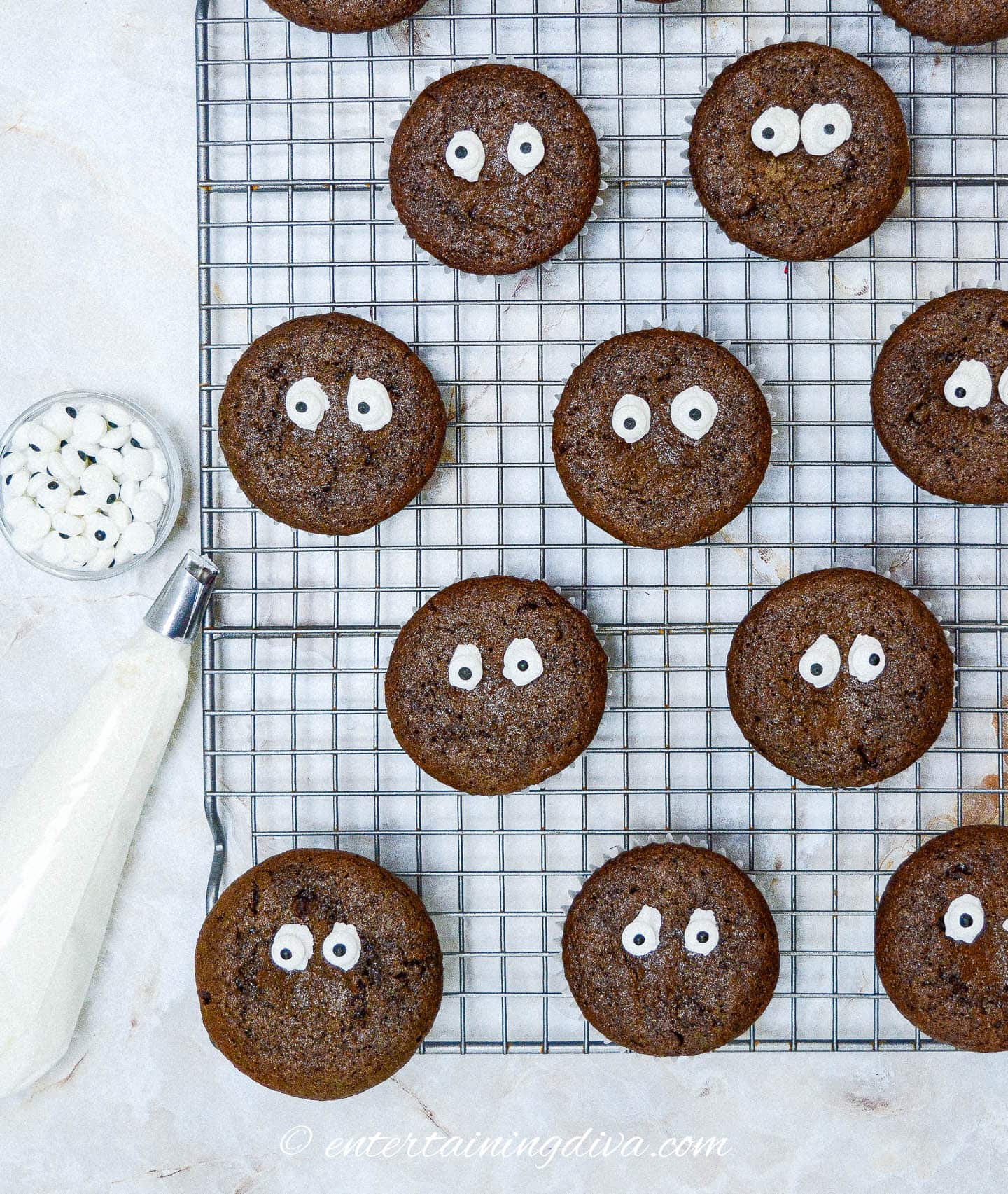 Chocolate cupcakes with candy eyes on a cooling rack.