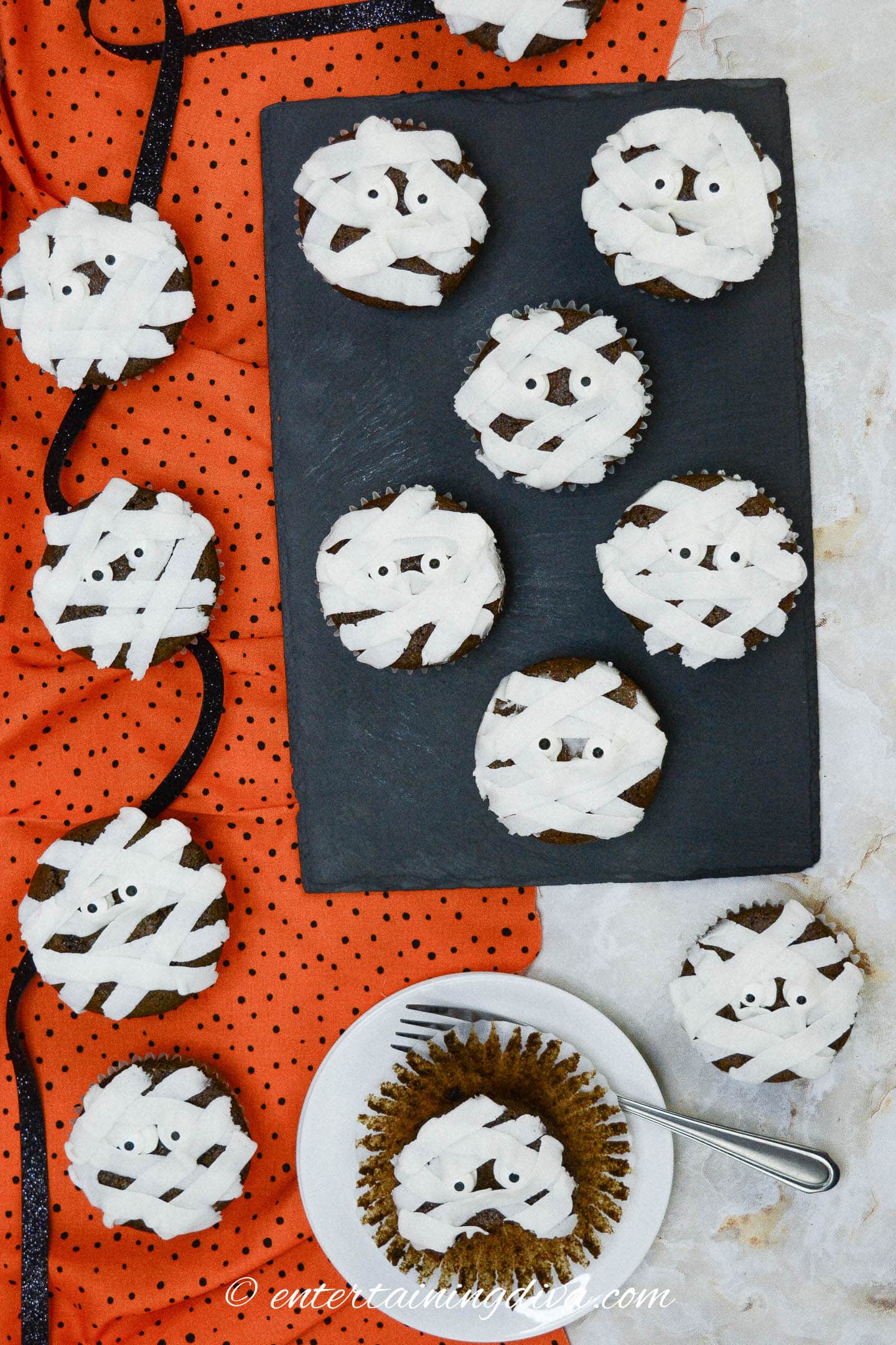 Mummy cupcakes with white frosting on a plate.
