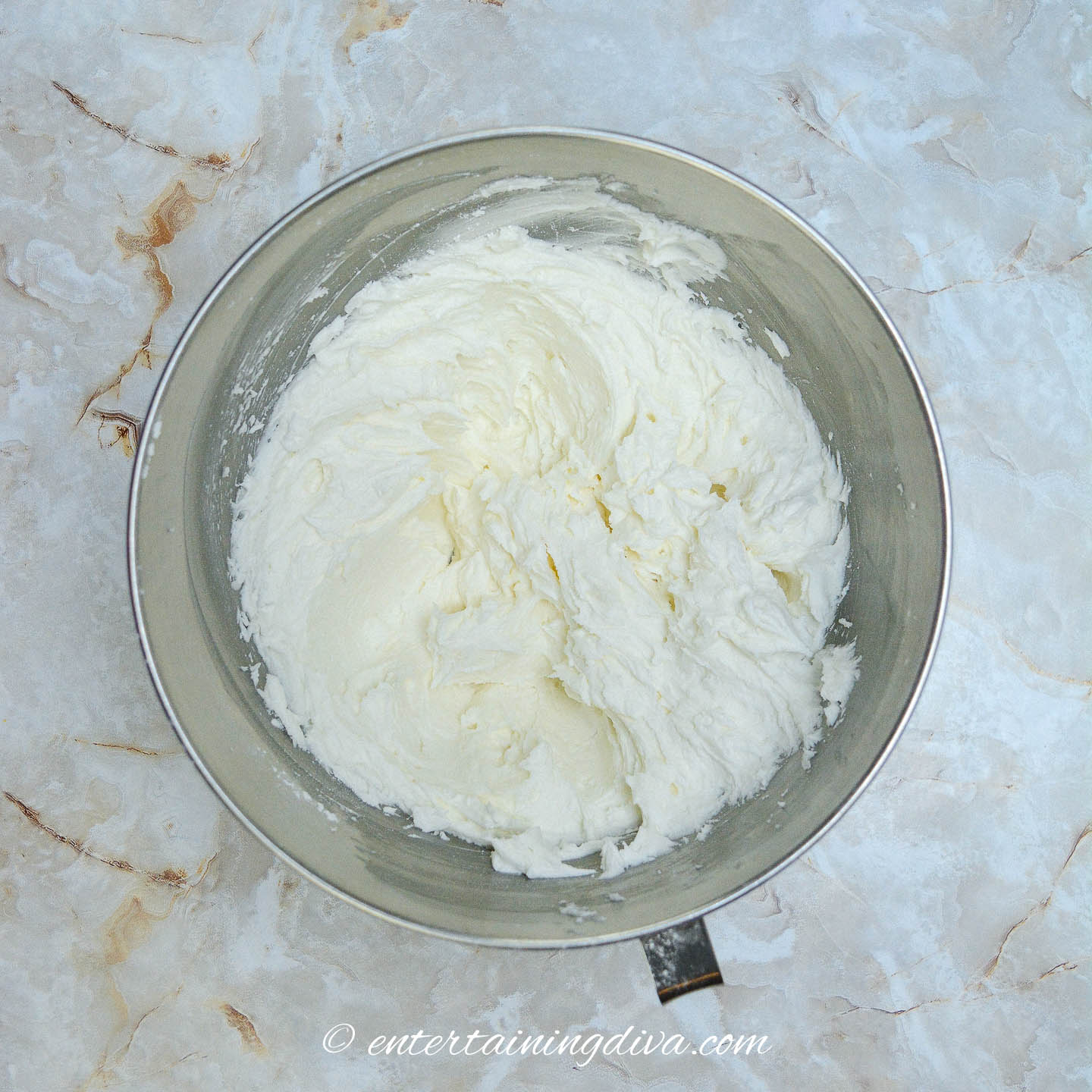 White frosting in a bowl on a marble countertop.