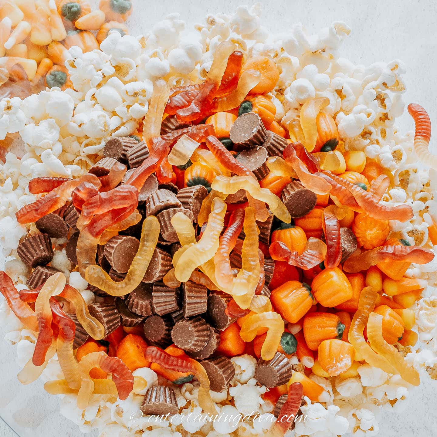 Popcorn, candy pumpkins, mini Reese's and gummy worms in a bowl