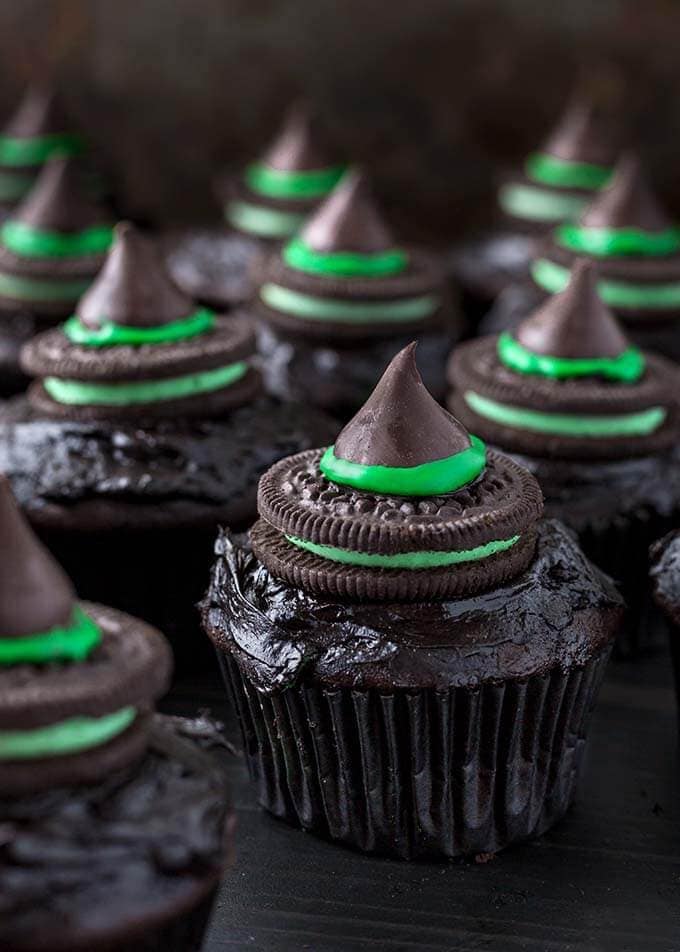 Chocolate cupcakes decorated with chocolate cookies, green icing, and chocolate kisses arranged to resemble witch hats.