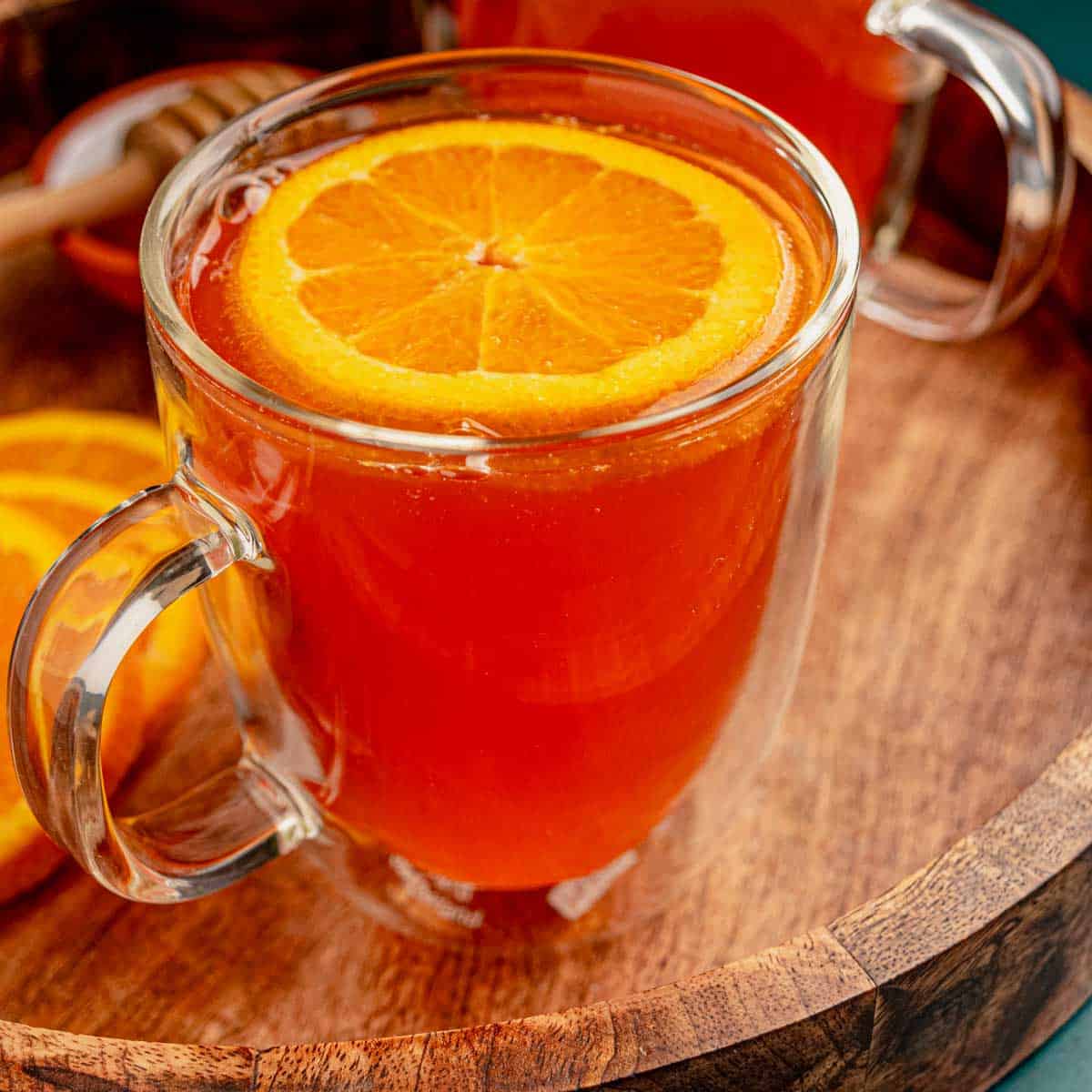 A cup of orange tea with slices of orange on a wooden tray.