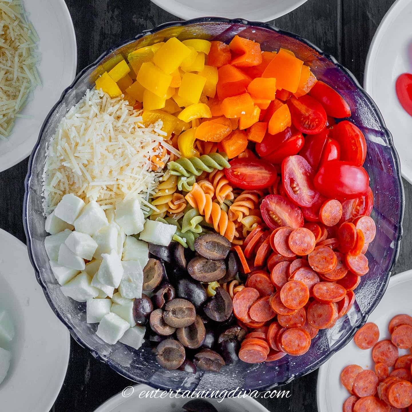 yellow peppers, orange peppers, cherry tomatoes, mini salami, black olives, mozzarella and parmesan on top of tricolor pasta in a bowl