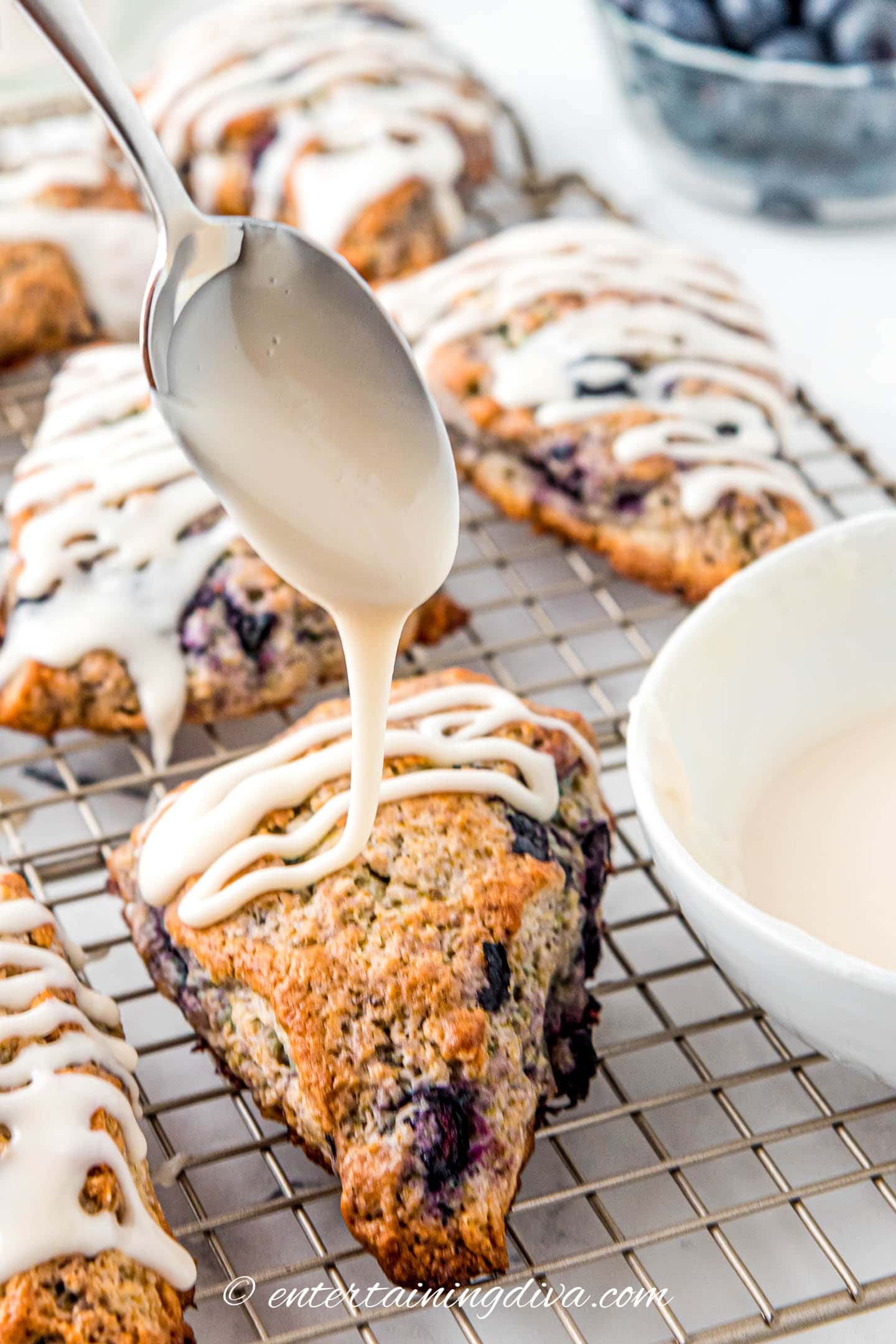 glaze being drizzled onto the top of a lemon blueberry scone with a spoon