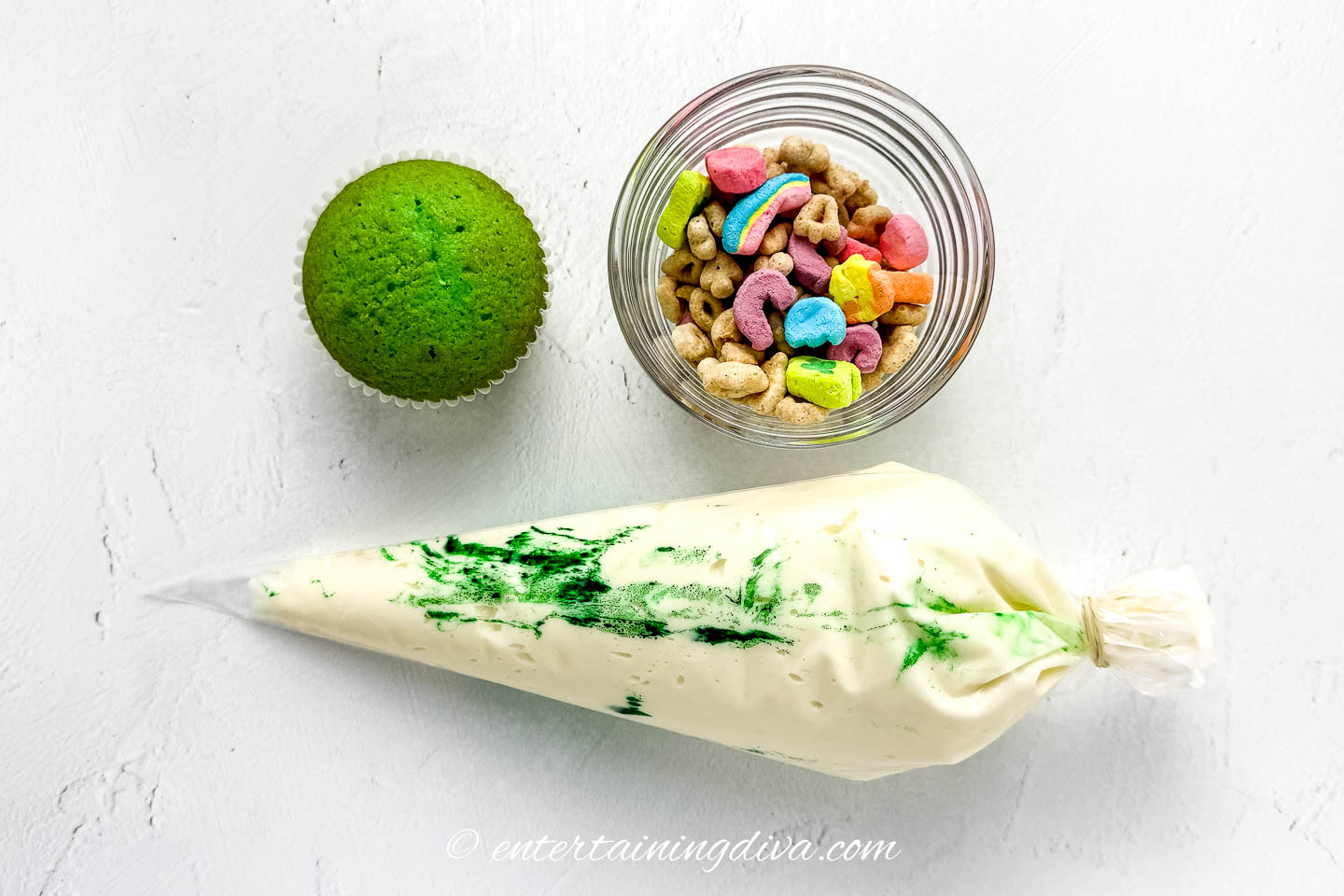 piping bag with frosting in it beside a green cupcake and a bowl of lucky charms