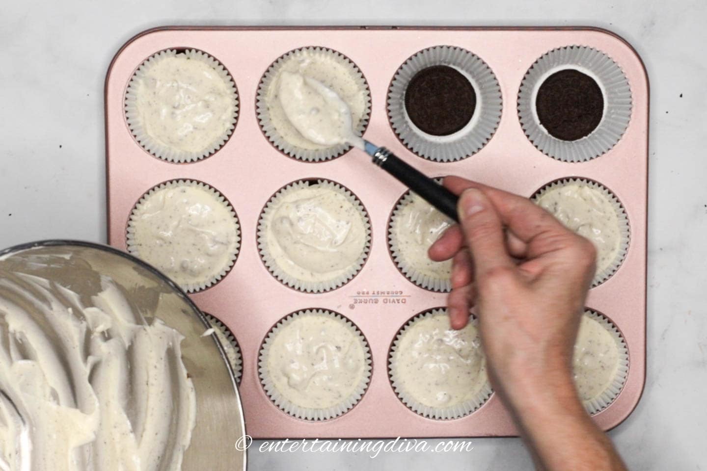 Cheesecake batter being spooned over the top of the Oreo cookie crust