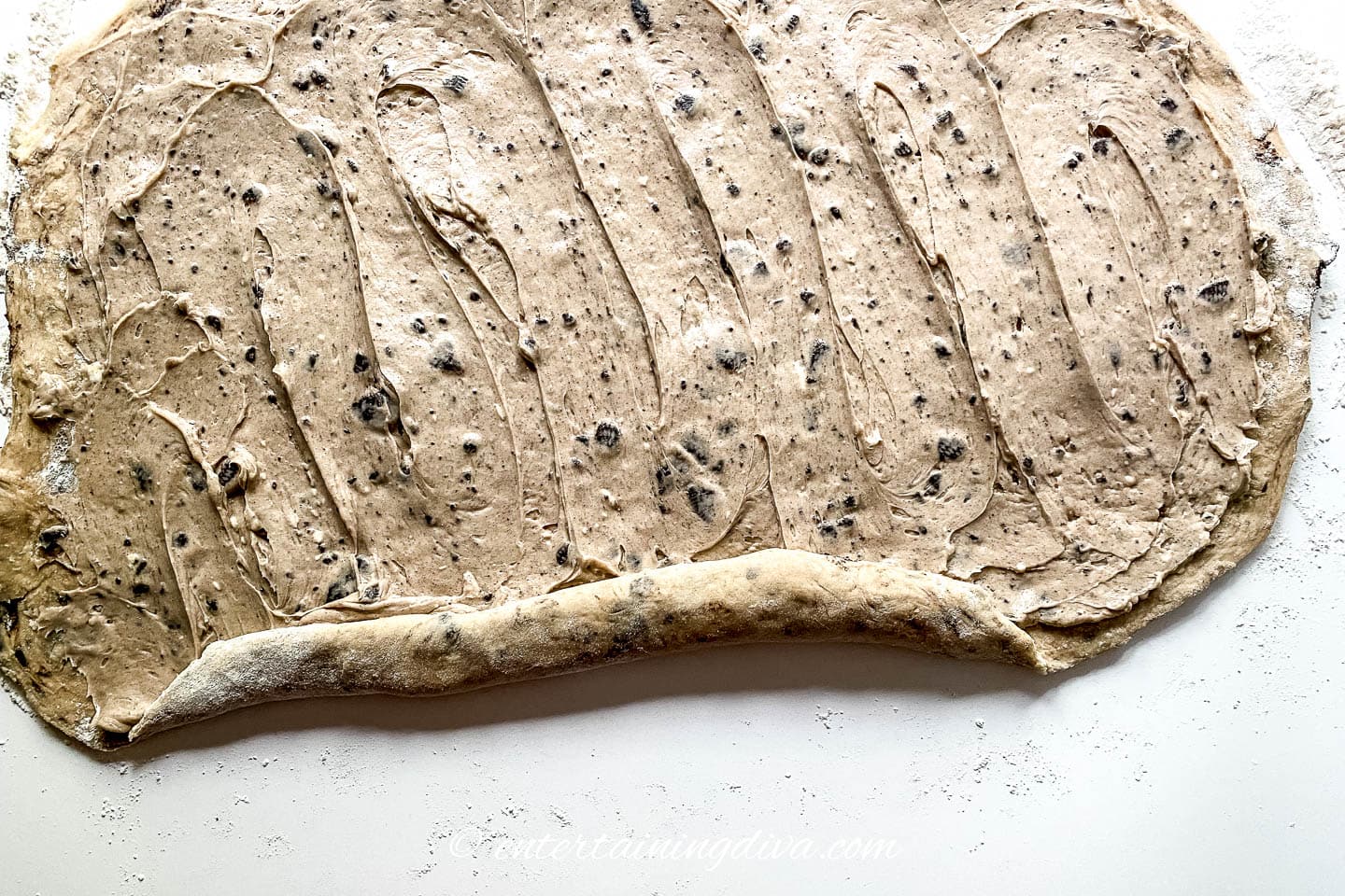 cinnamon roll dough rolled out with oreo cheesecake filling spread out on top of it