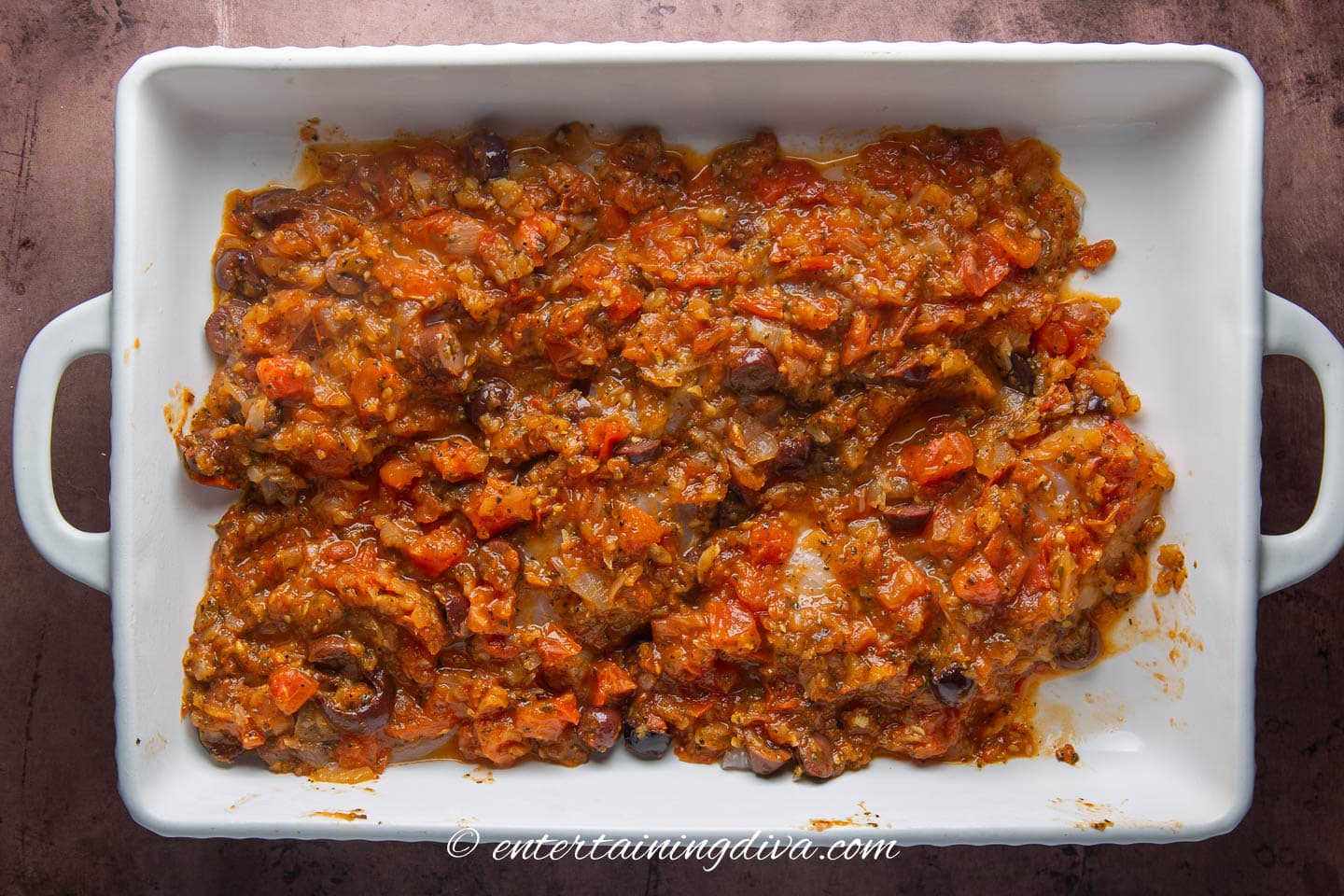 Tilapia fillets covered with tomato sauce with olives in a baking dish