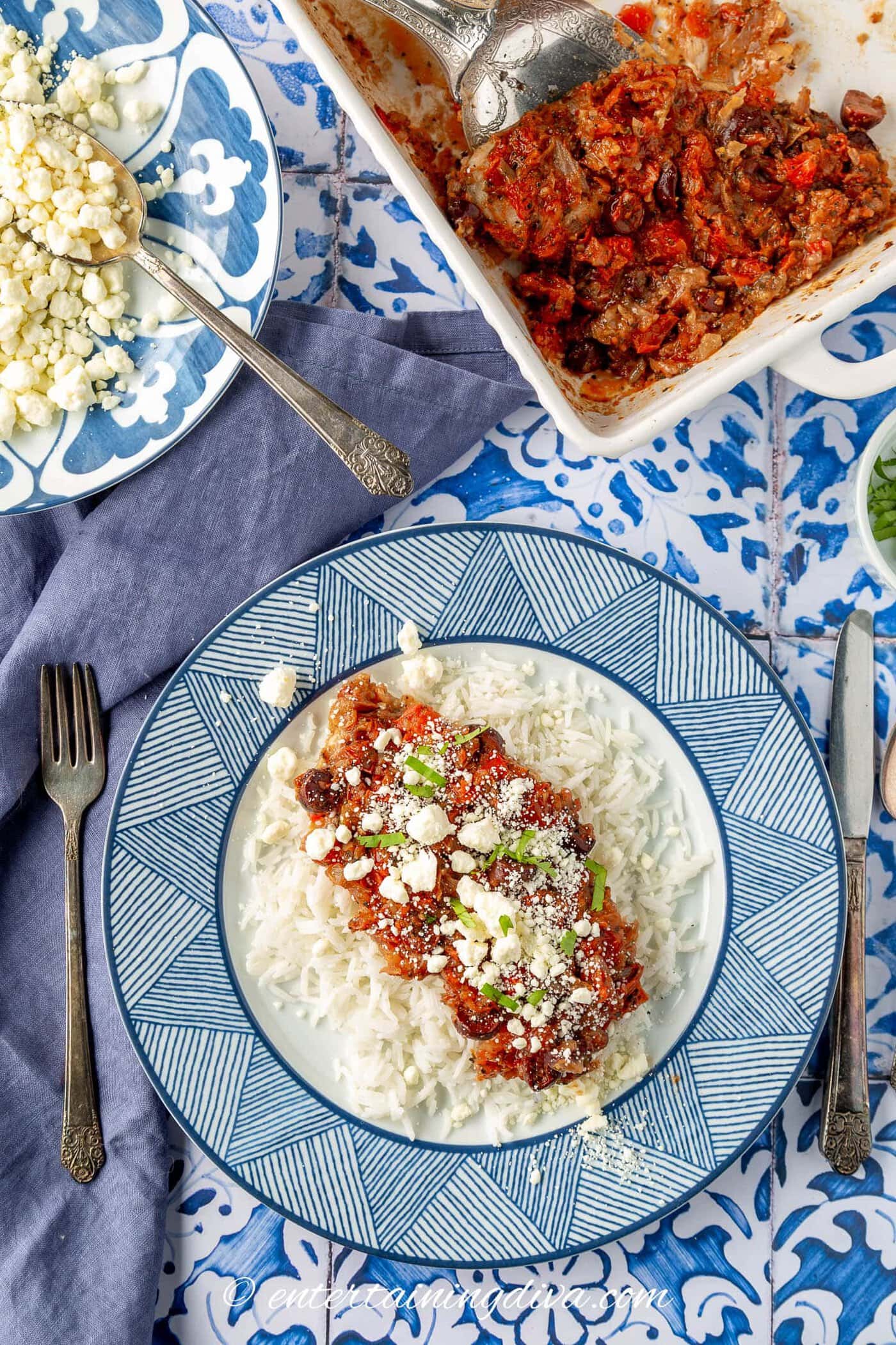 Oven baked Greek tilapia on a plate beside a bowl of feta cheese and a baking dish