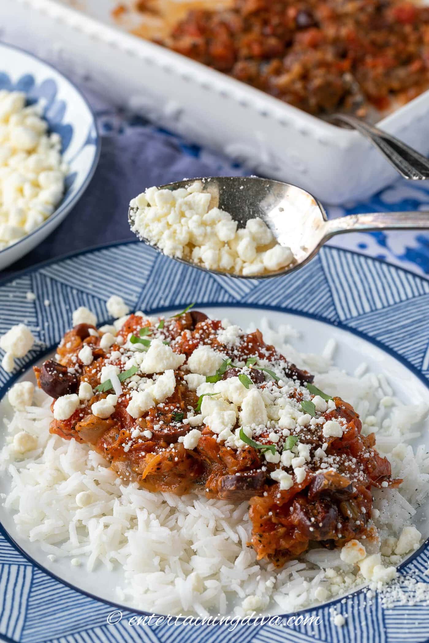Feta cheese being sprinkled over tilapia with tomatoes and olives