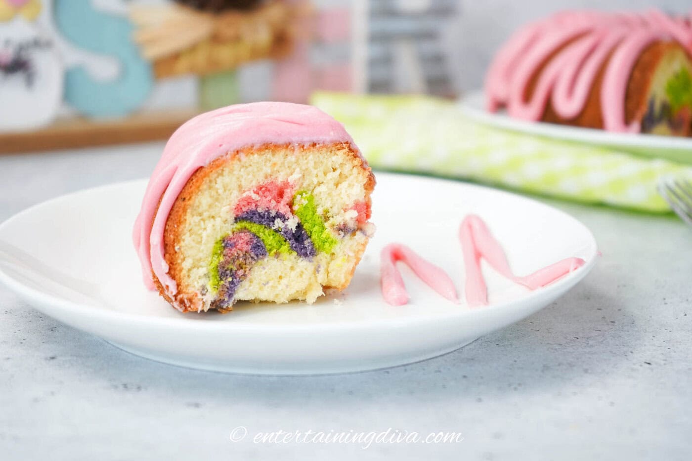 a slice of pastel swirled bundt cake with pink frosting on a plate