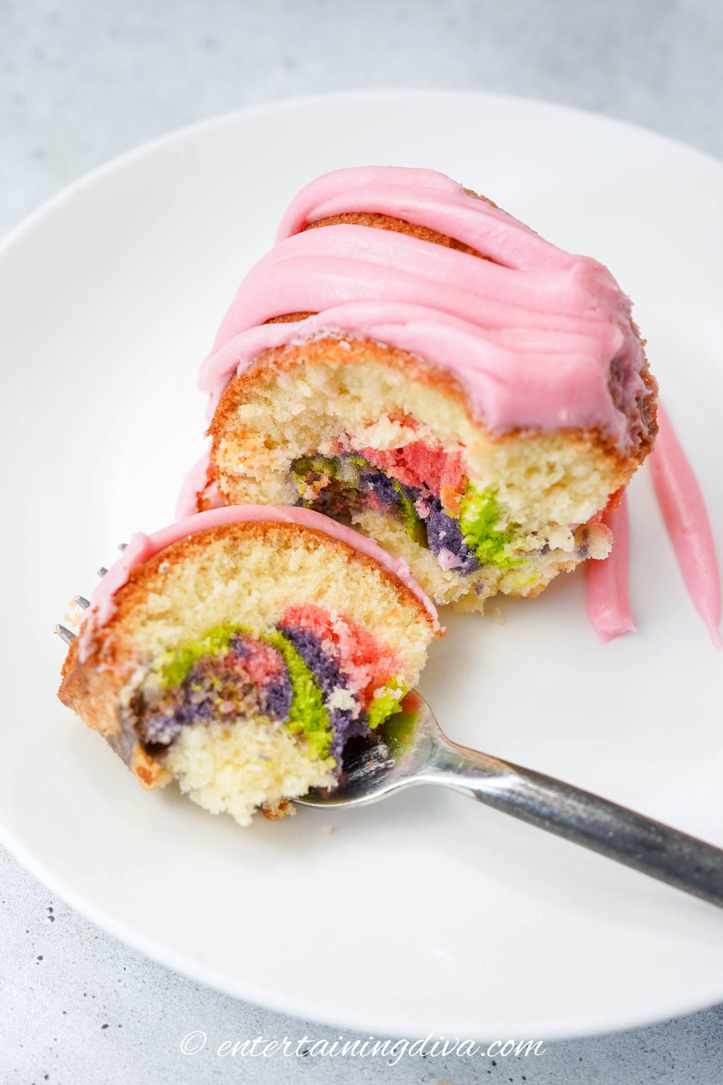 a fork with a piece of pastel swirled bundt cake beside the rest of the slice on a plate