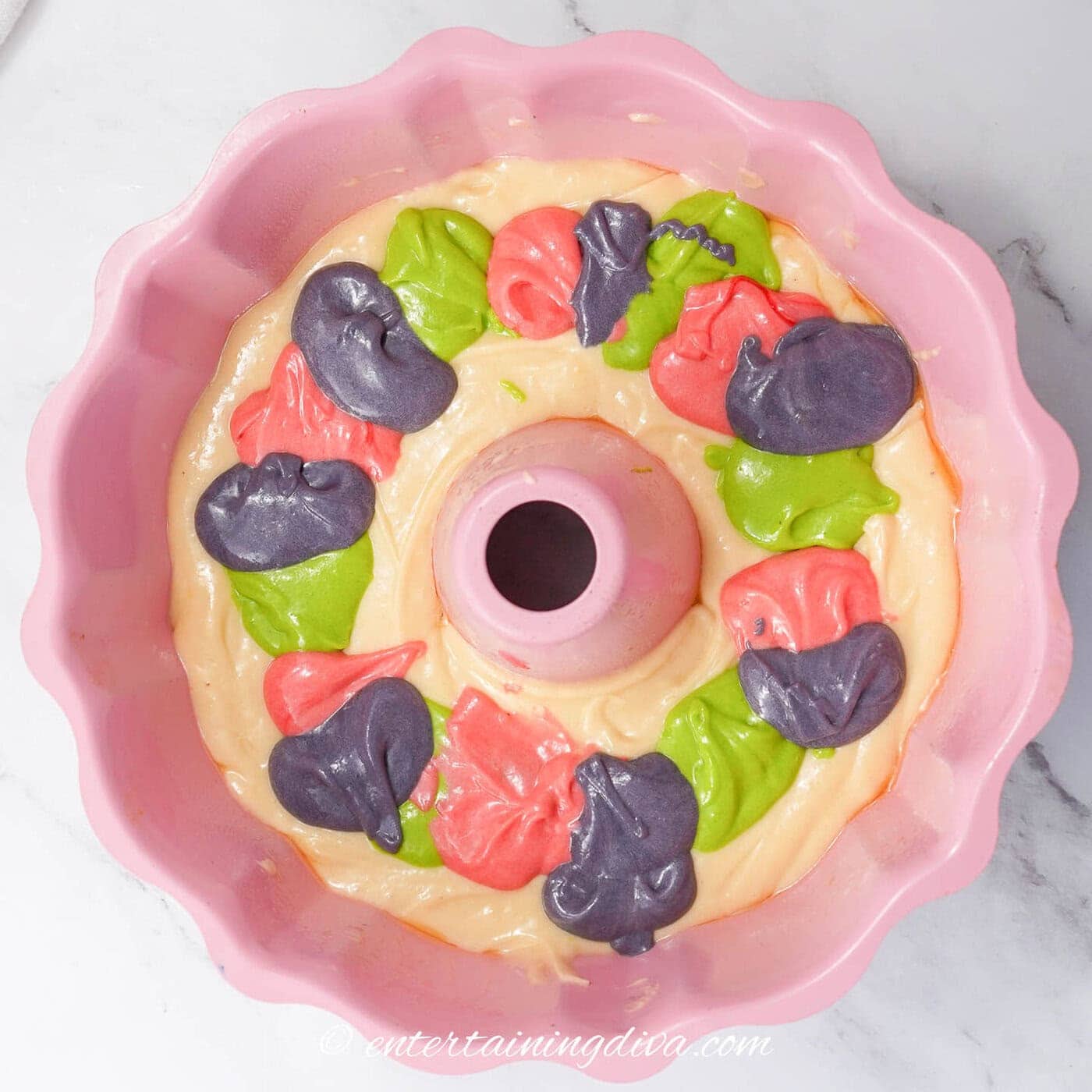 a bundt cake with dollops of purple, green and pink batter around the middle