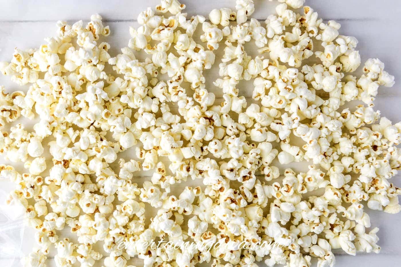A scattered layer of plain popcorn spread out on a light-colored surface.