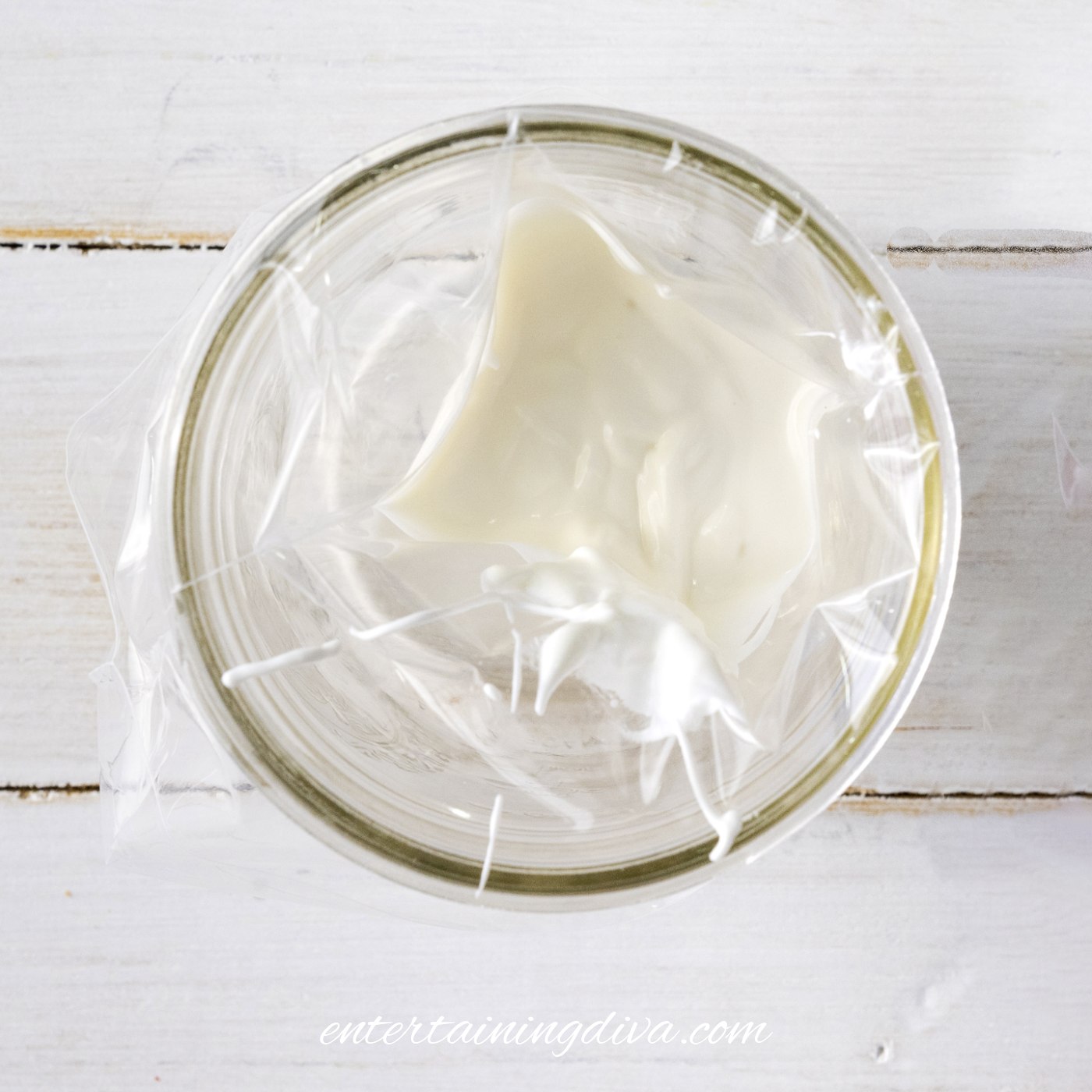 A glass lined with a piping bag filled with melted white candy melts.