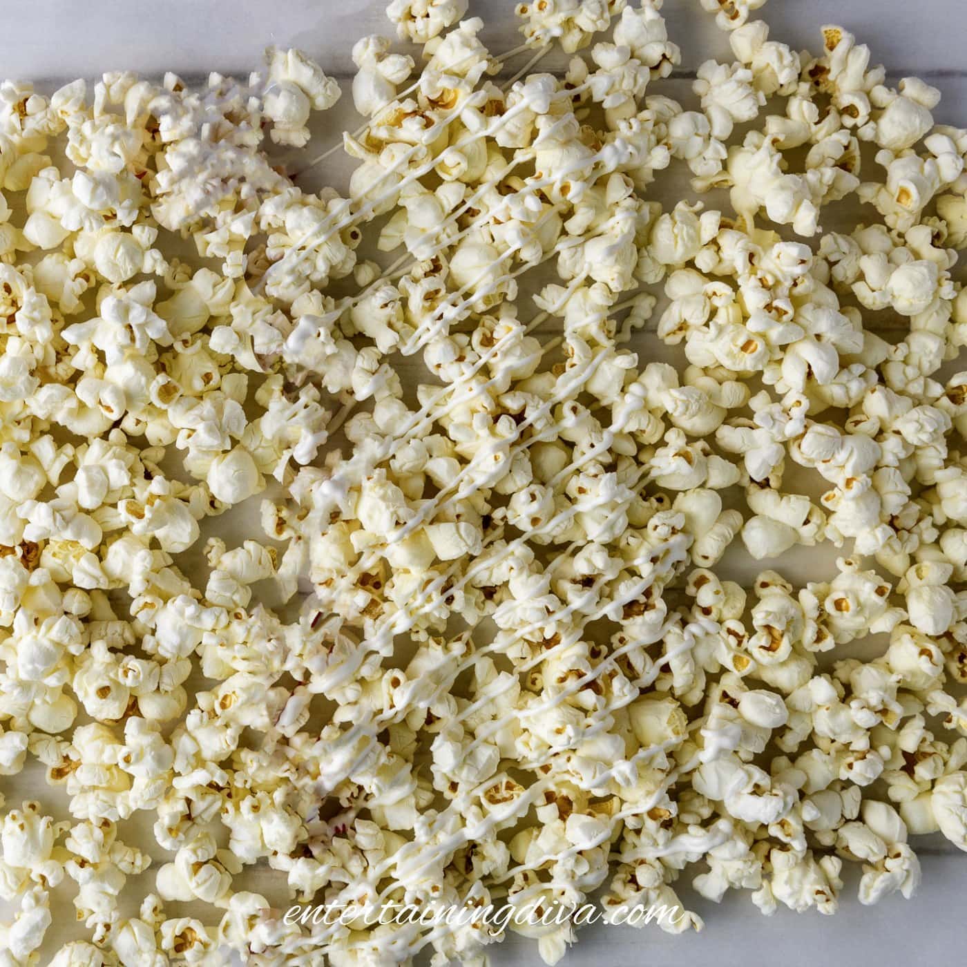 Popcorn spread out on parchment paper, drizzled with white candy melts.