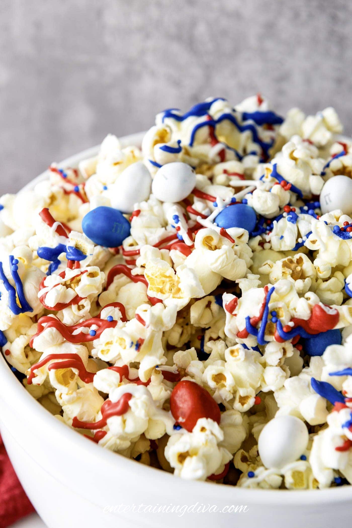A bowl of popcorn topped with red, white, and blue candy-coated chocolates, red and blue drizzle, and sprinkles.
