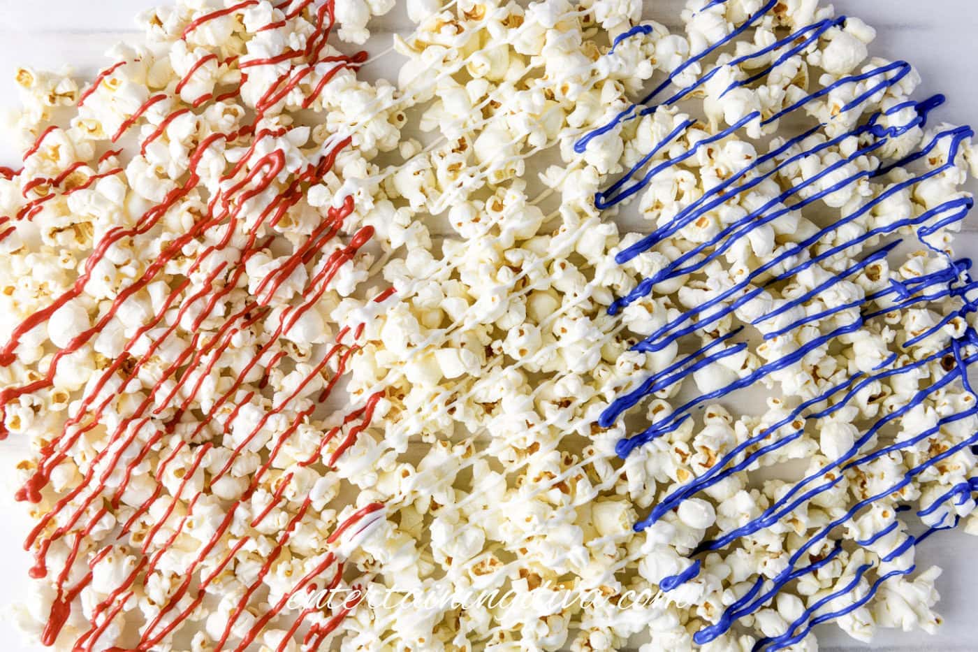 Popcorn spread out on a surface with red, white, and blue candy drizzle arranged in diagonal stripes.