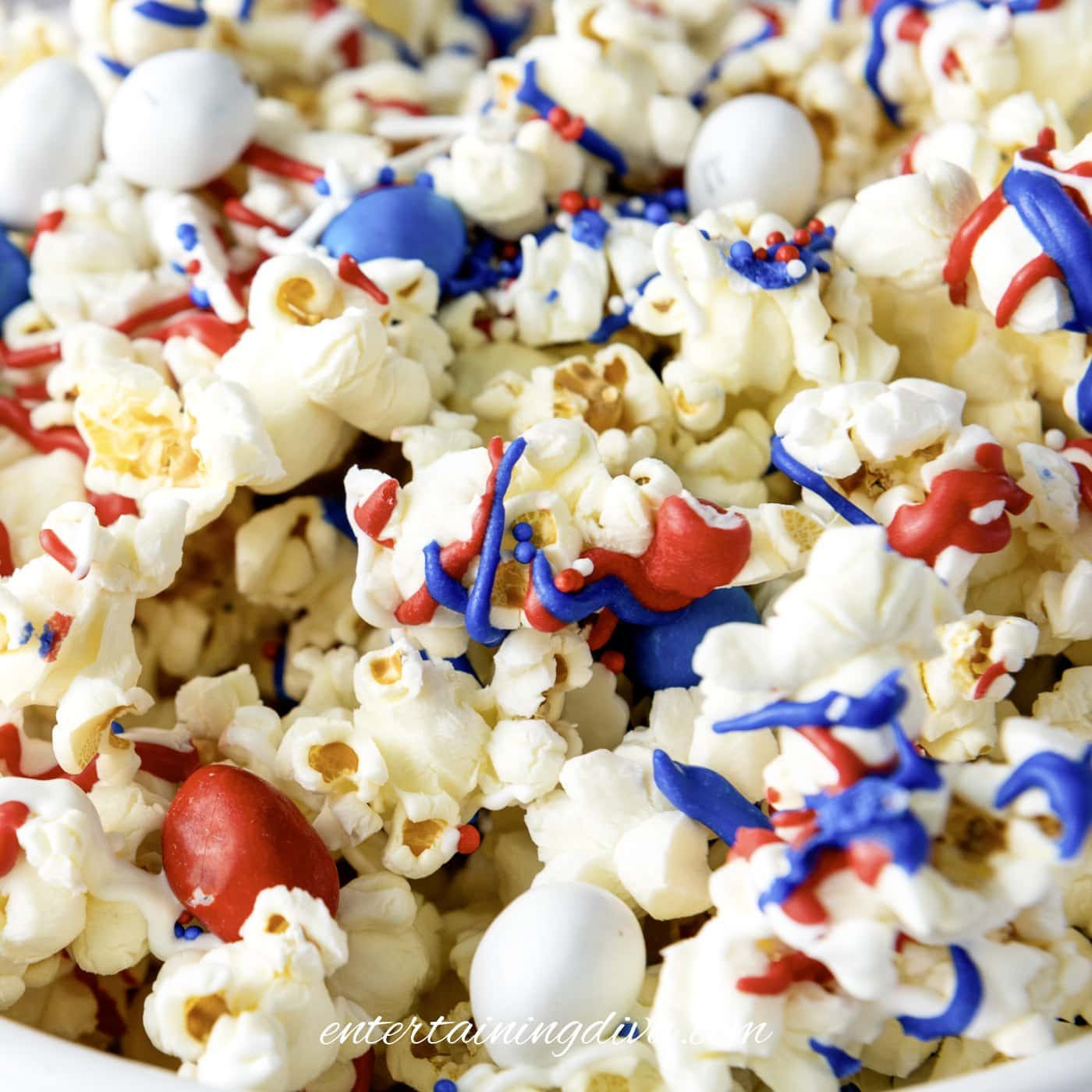 A close-up of popcorn topped with red, white, and blue candies and drizzled with matching colored icing.