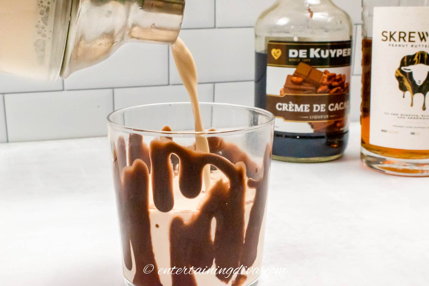 peanut butter cup cocktail being poured into a rocks glass drizzled with chocolate syrup
