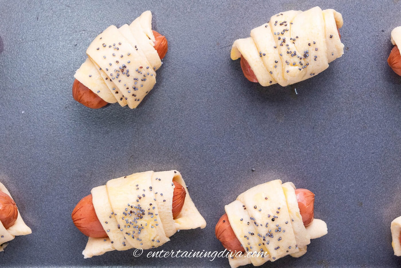 pigs in a blanket garnished with poppy seeds on a baking sheet
