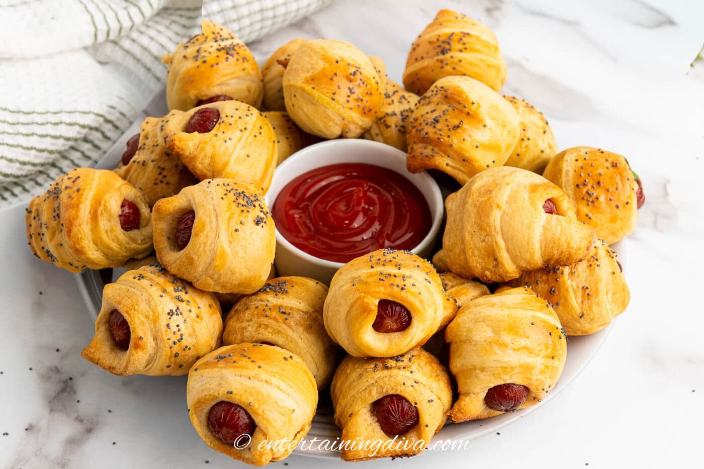side view of pigs in a blanket on a plate with ketchup in the middle