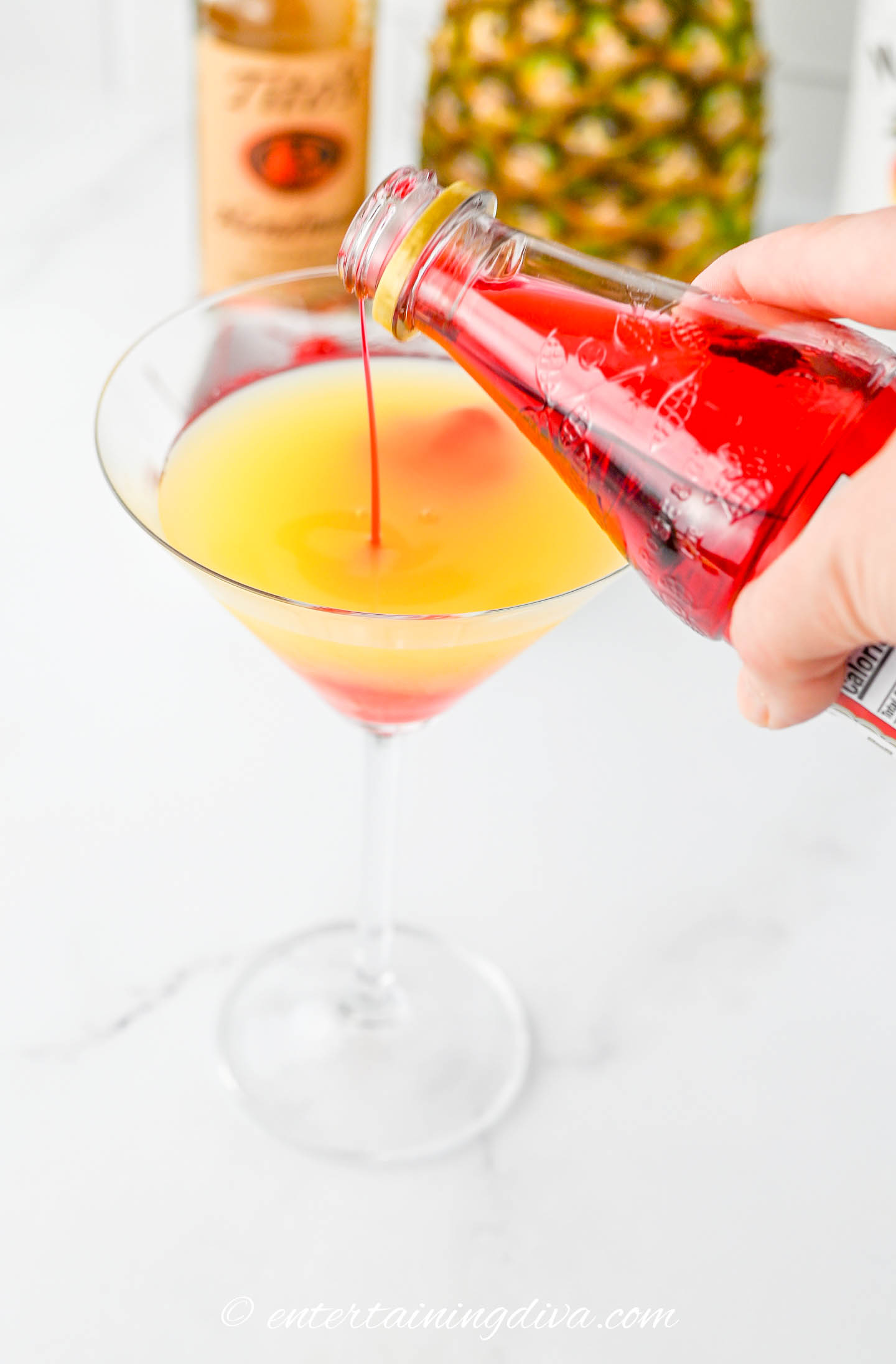 grenadine being poured into a pineapple upside down cake cocktail