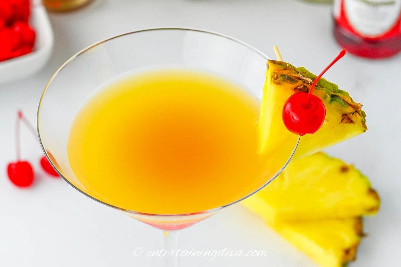 The pineapple and maraschino garnish on the rim of a pineapple upside down cake drink