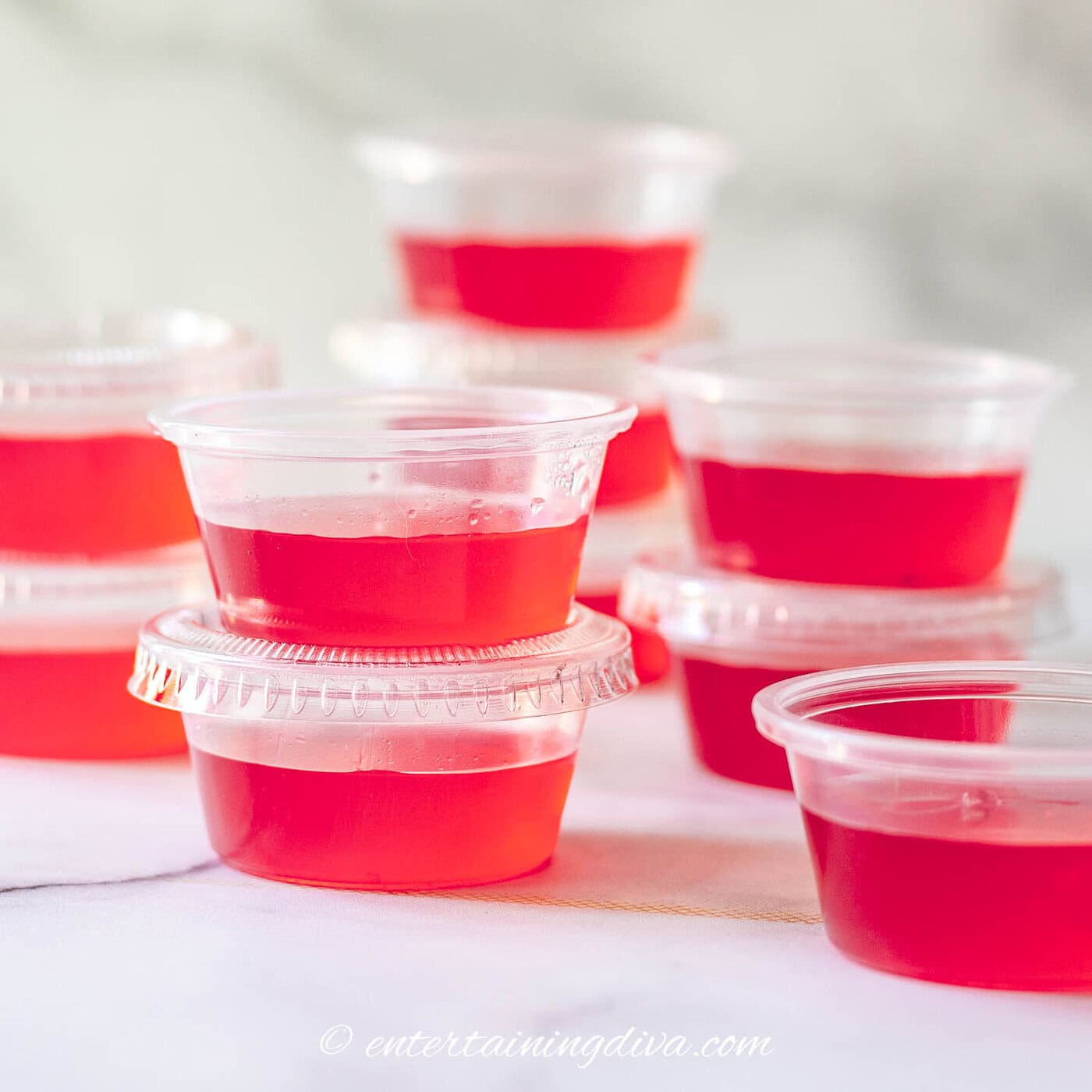 Several small plastic containers filled with red gelatin are stacked on a white surface.