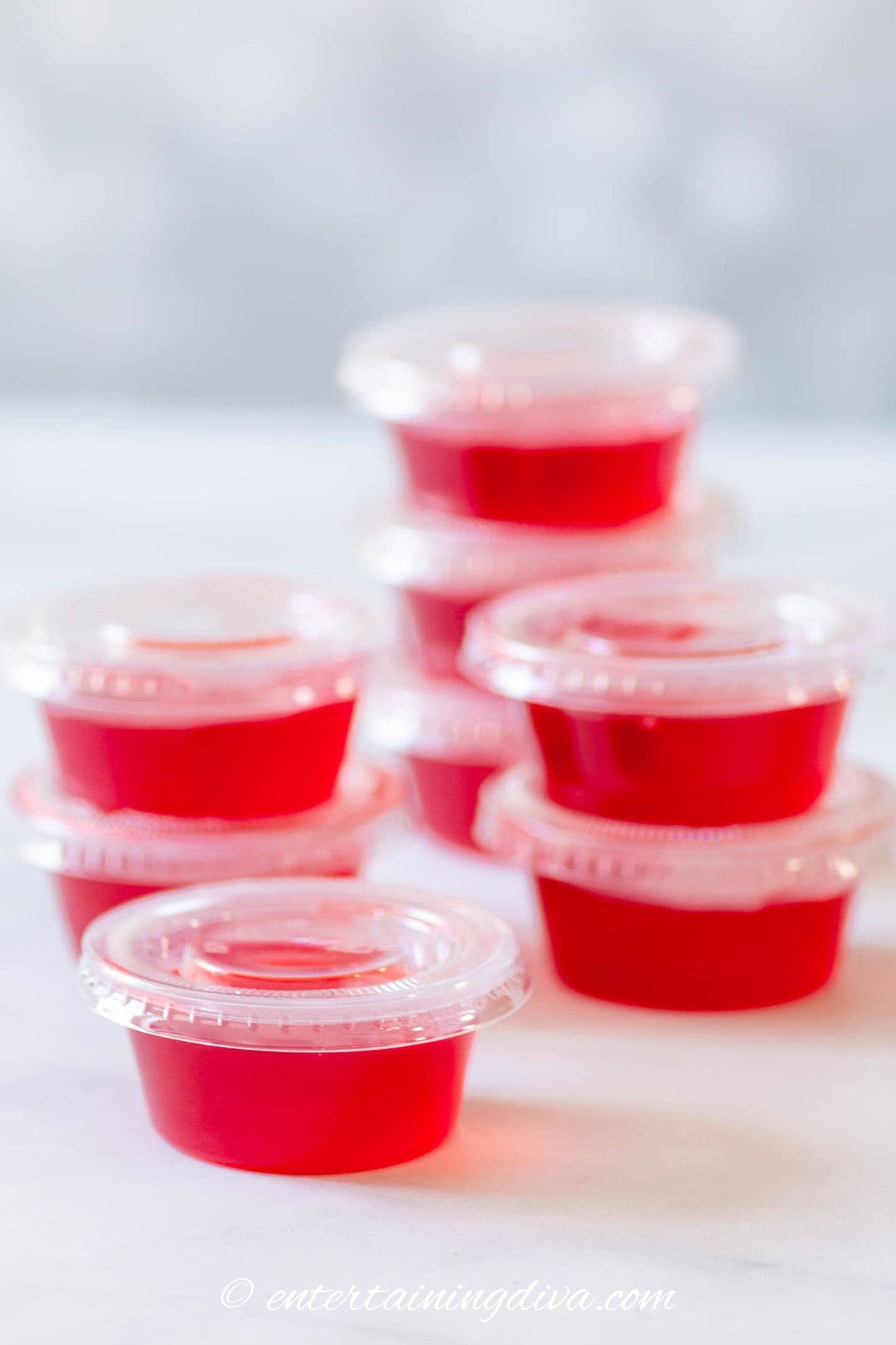 a stack of raspberry lemonade jello shots in jello shot cups with lids