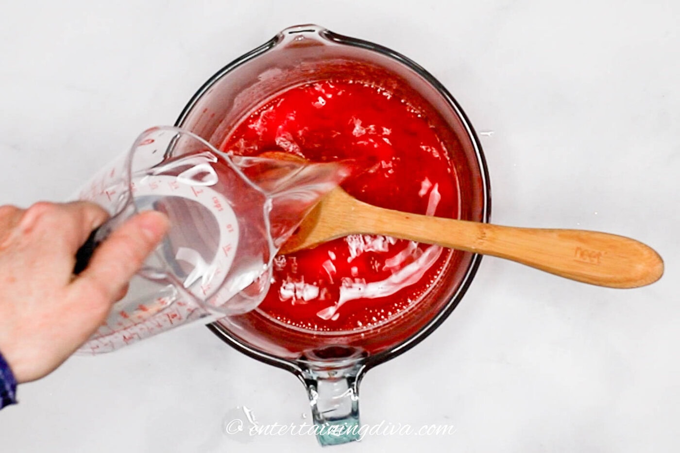 hot water being poured into raspberry jello in a bowl