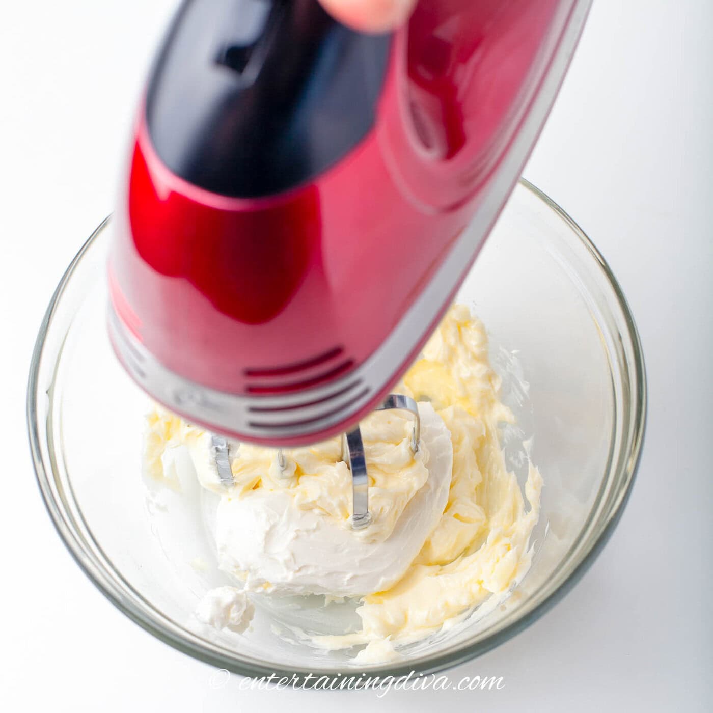 cream cheese and butter being mixed in a bowl with a mixer